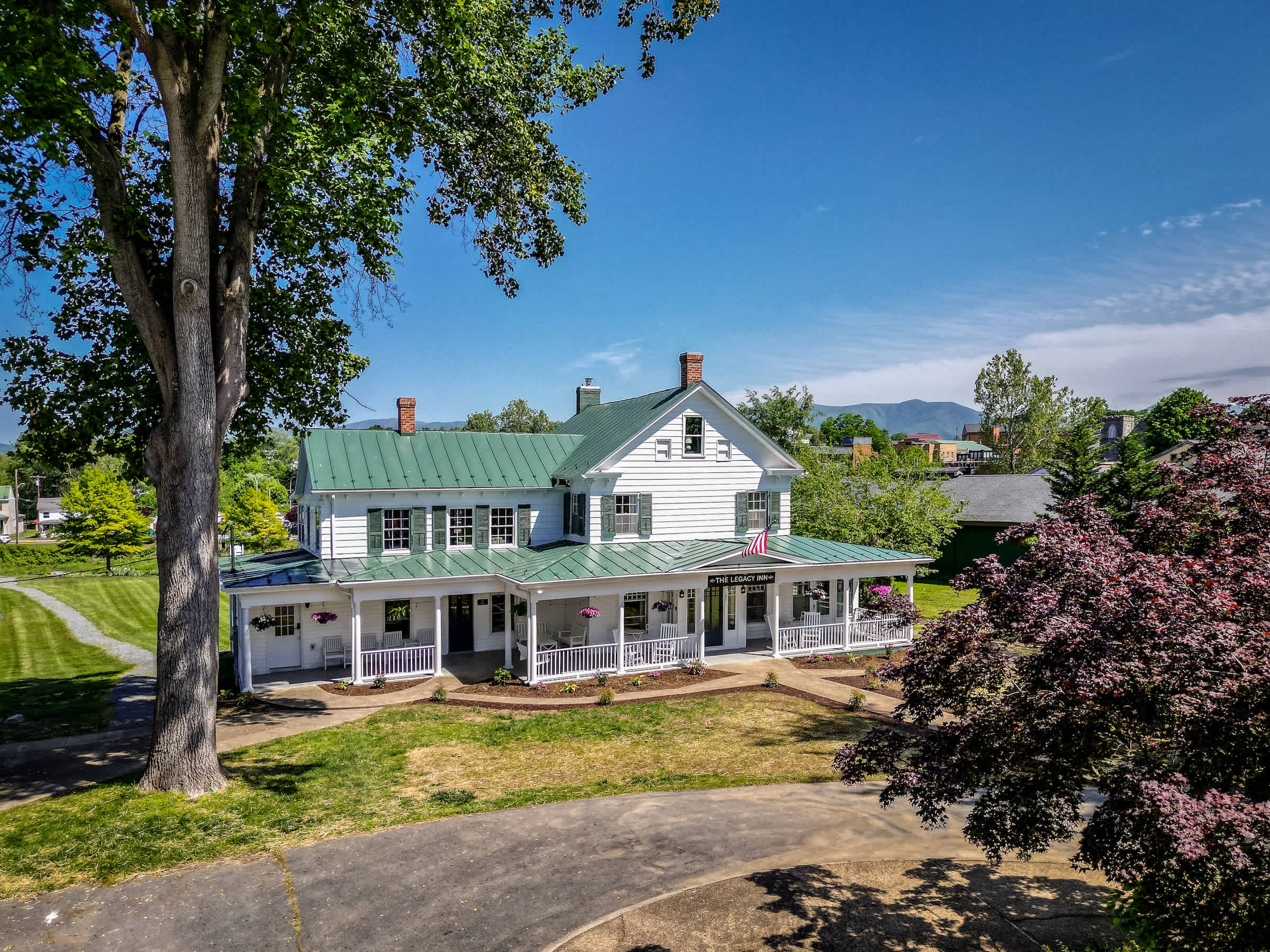 Historic inn with a green metal roof and wraparound porch surrounded by trees and mountain views