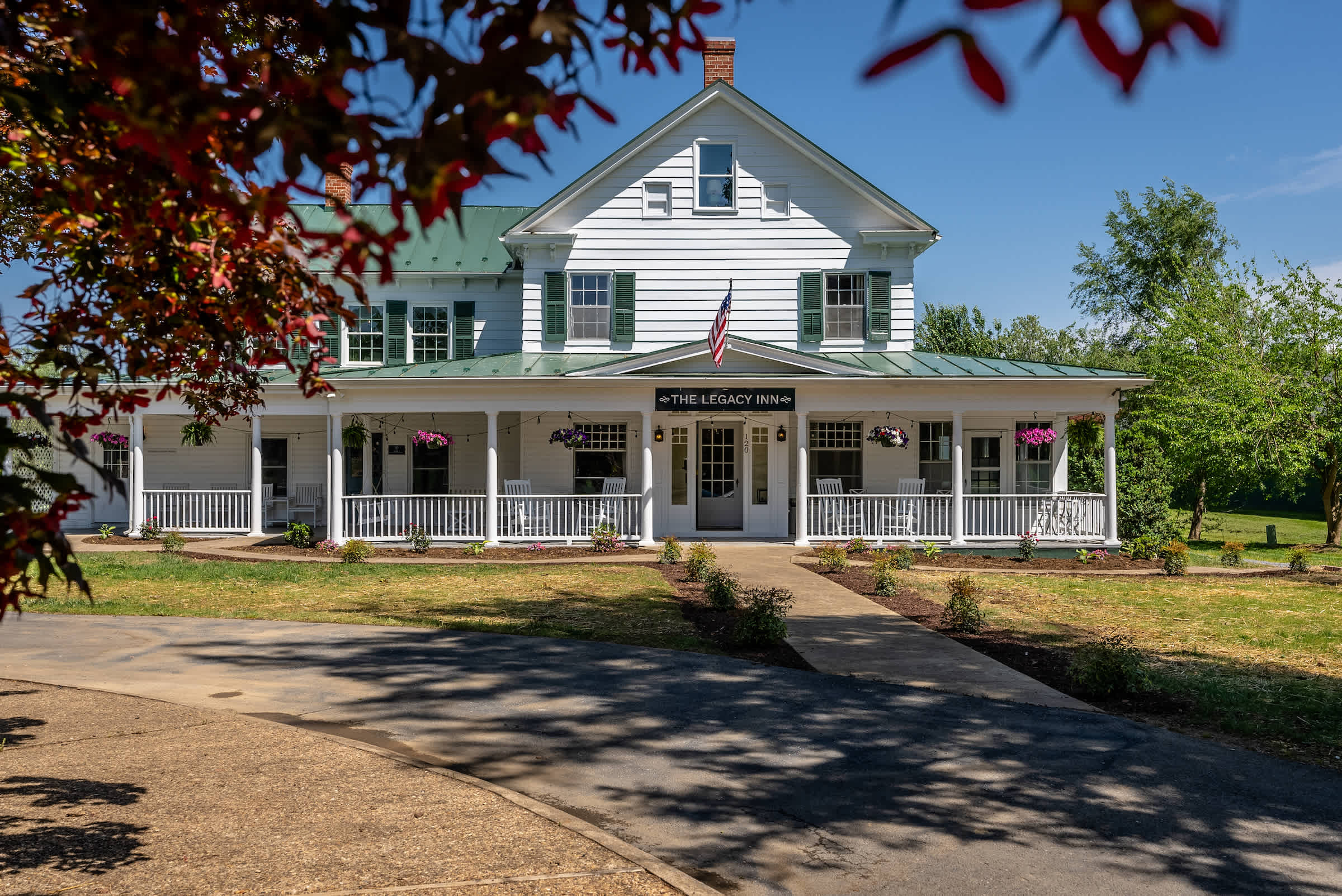 Historic inn with a spacious porch and rocking chairs surrounded by greenery.