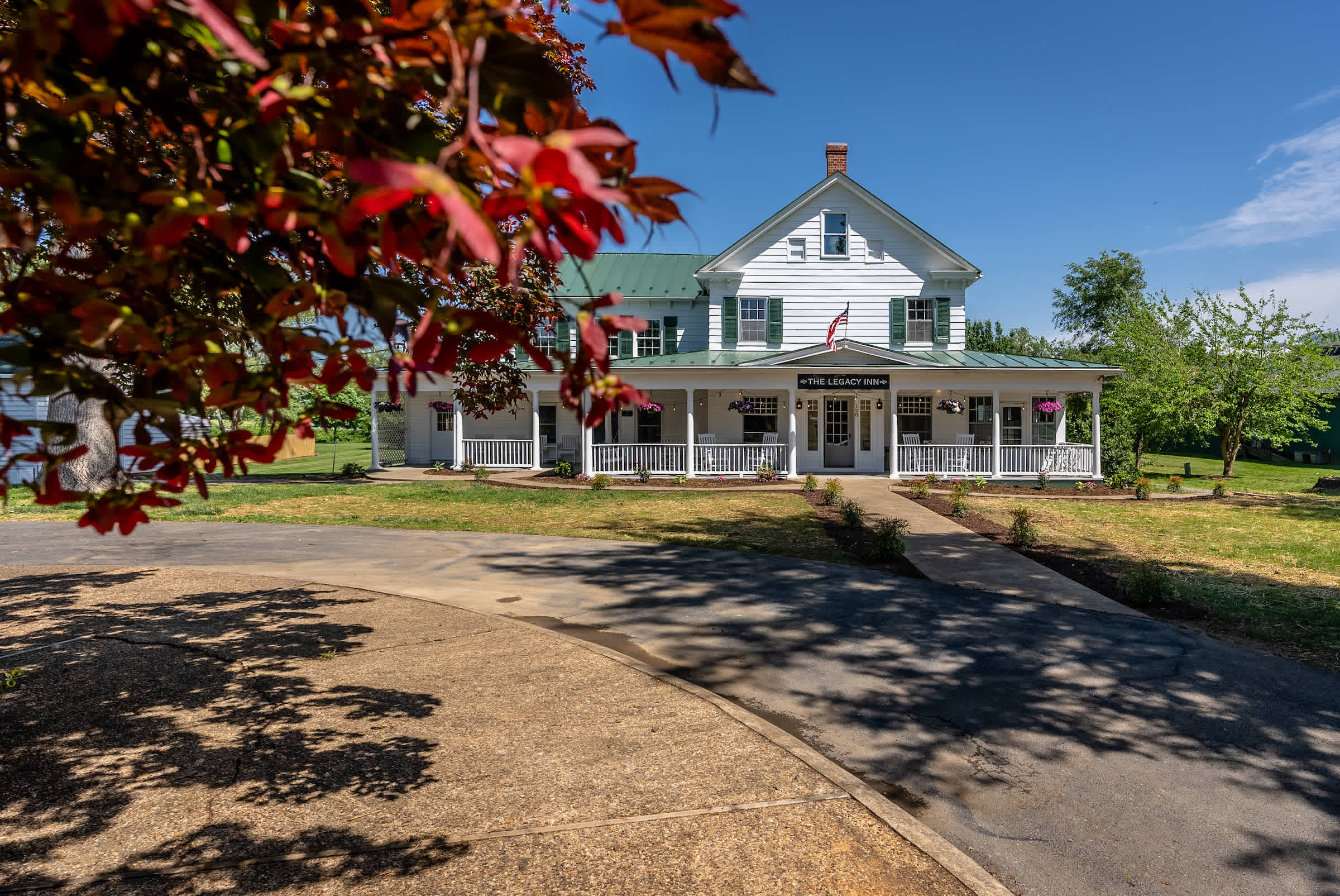 Historic inn with a spacious front porch surrounded by greenery and clear blue skies