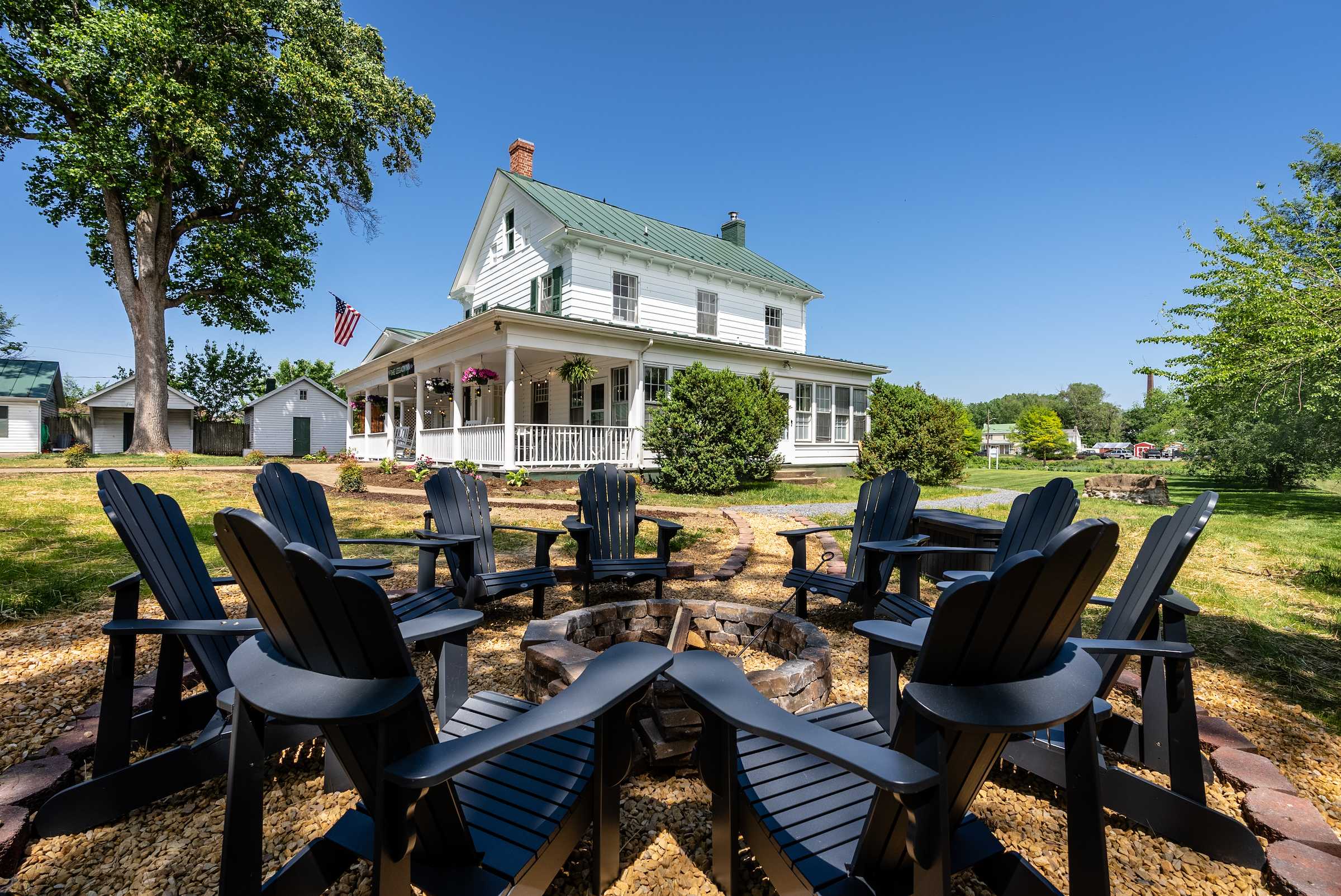 Outdoor fire pit area with seating in front of a classic white farmhouse.