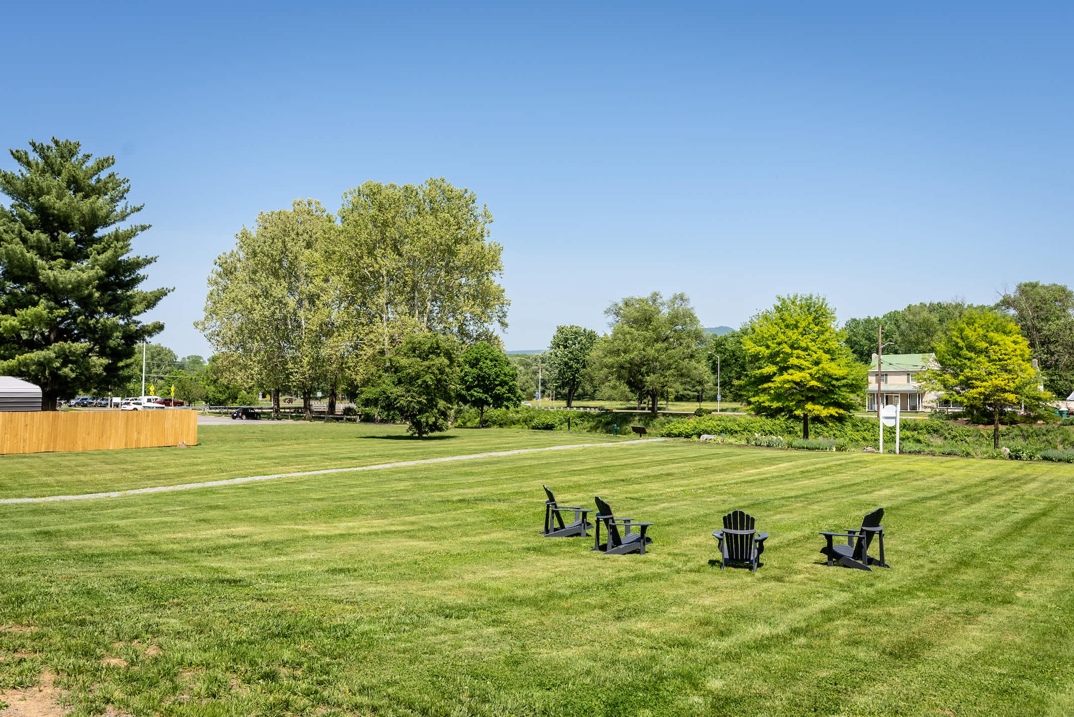 Open green lawn with seating area surrounded by mature trees under a clear blue sky