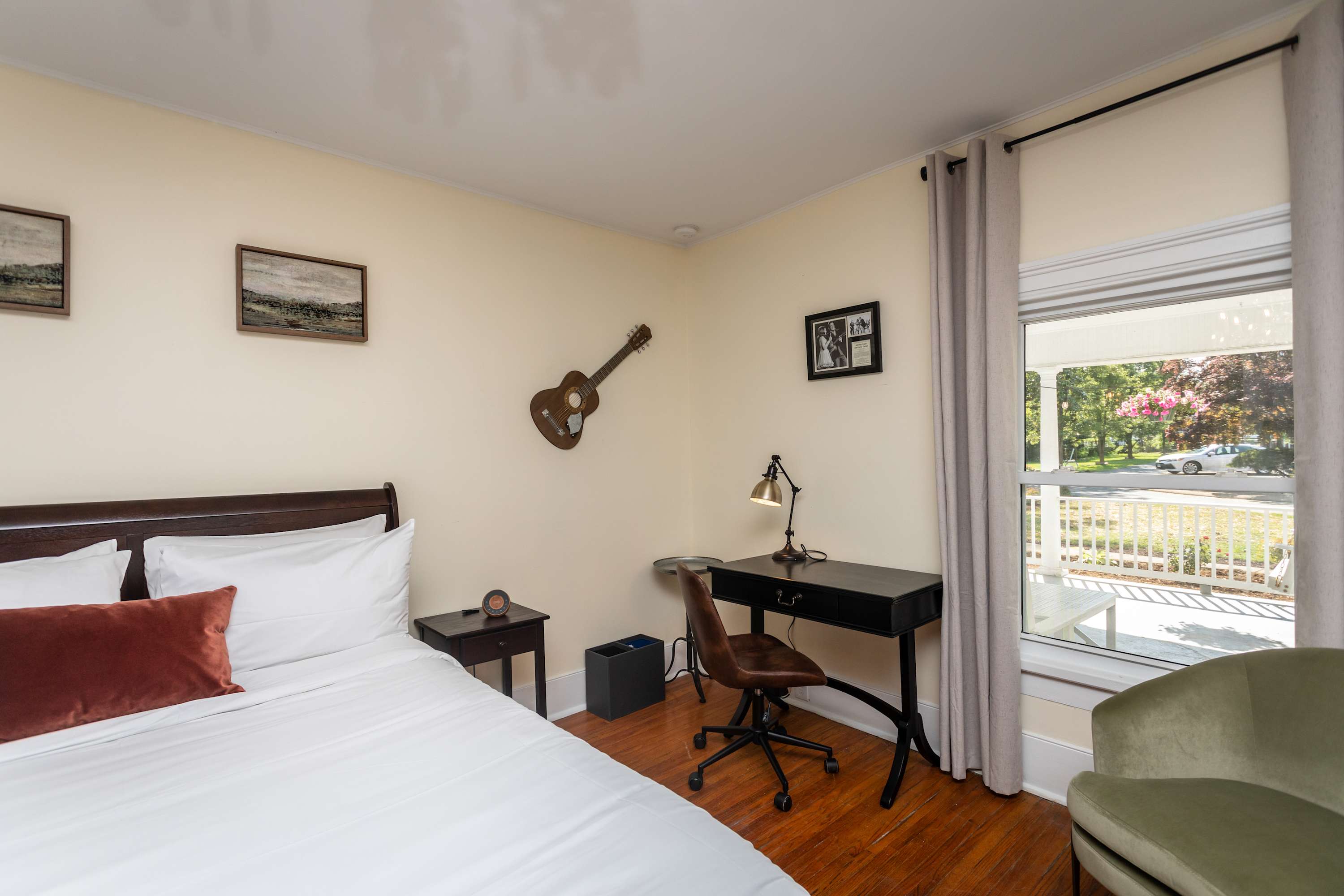 A bright bedroom with a work desk and a window overlooking the porch and garden.
