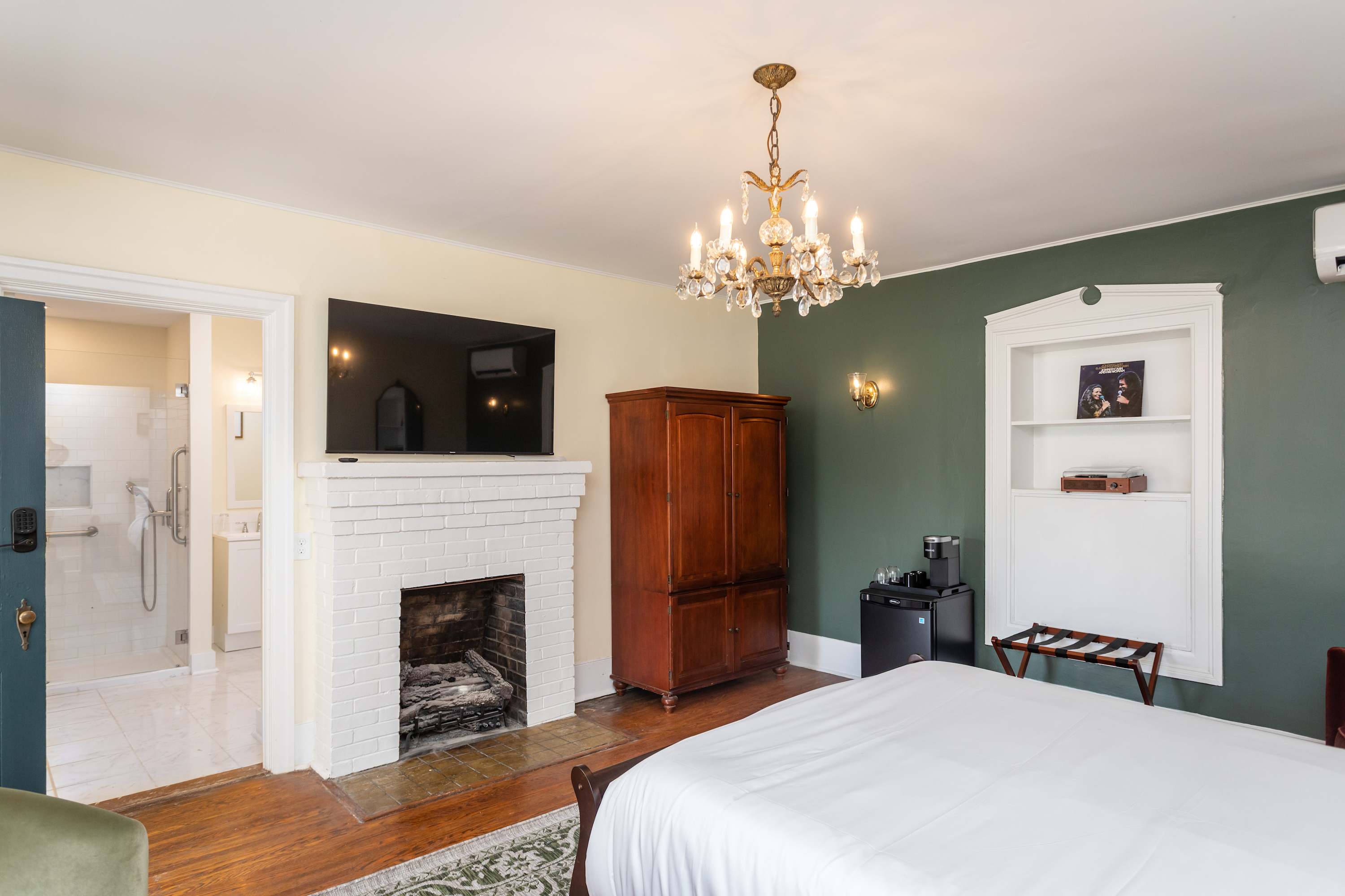 Relax in this cozy room featuring a classic chandelier, white brick fireplace, and a vintage wooden armoire.