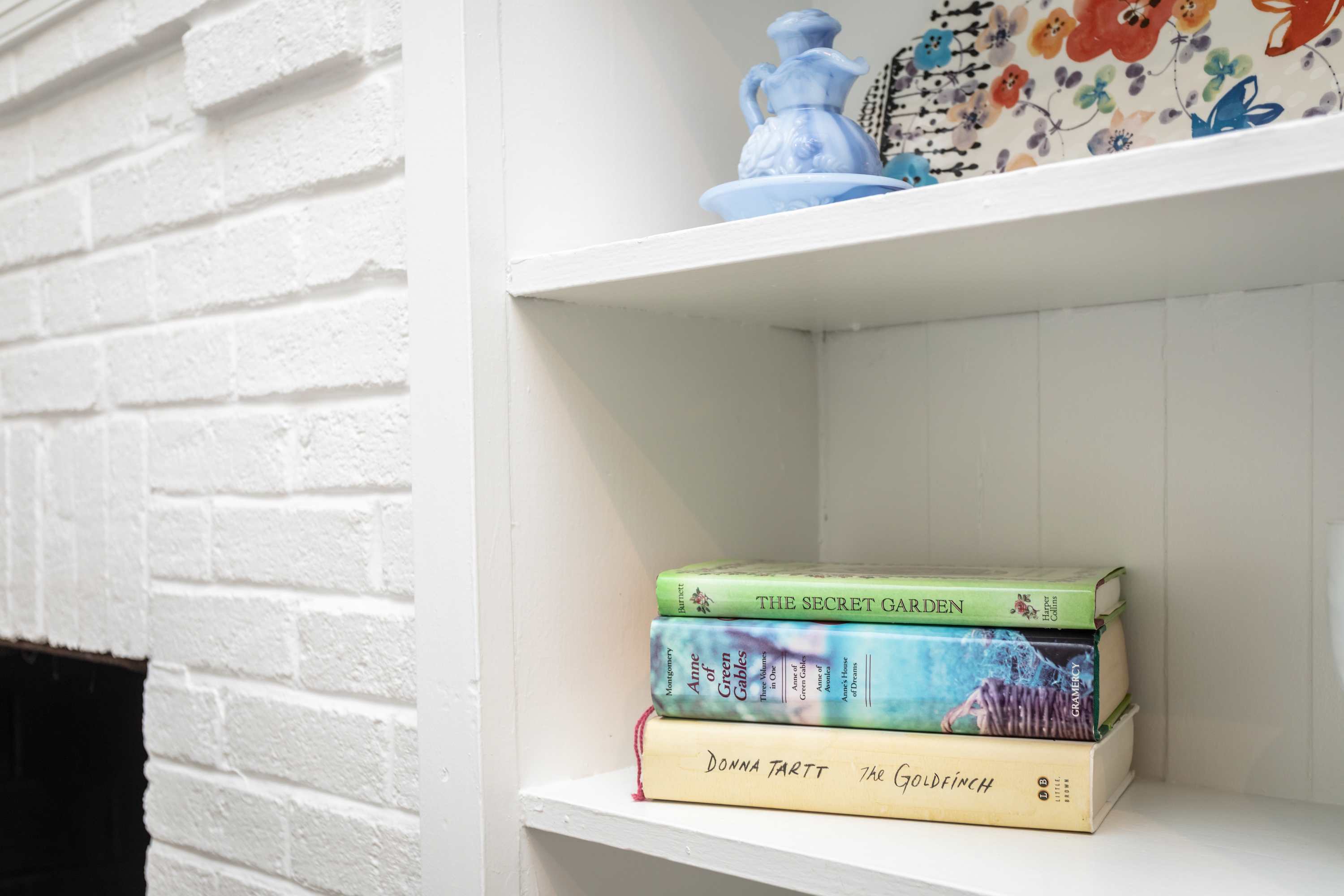 A cozy shelf featuring classic novels and a decorative blue pitcher against a white brick wall.