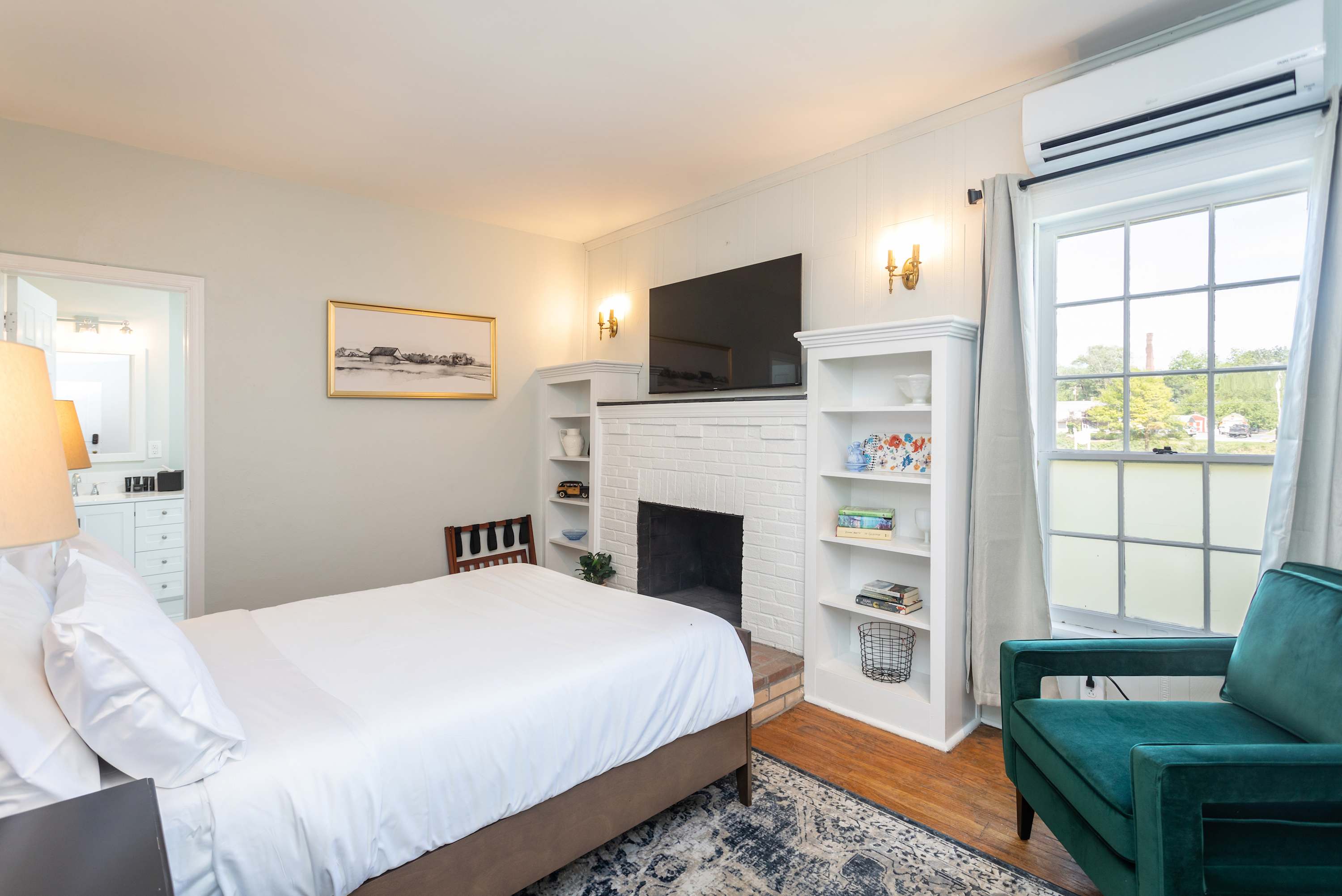 Bright bedroom with a white brick fireplace and a large window offering natural light.