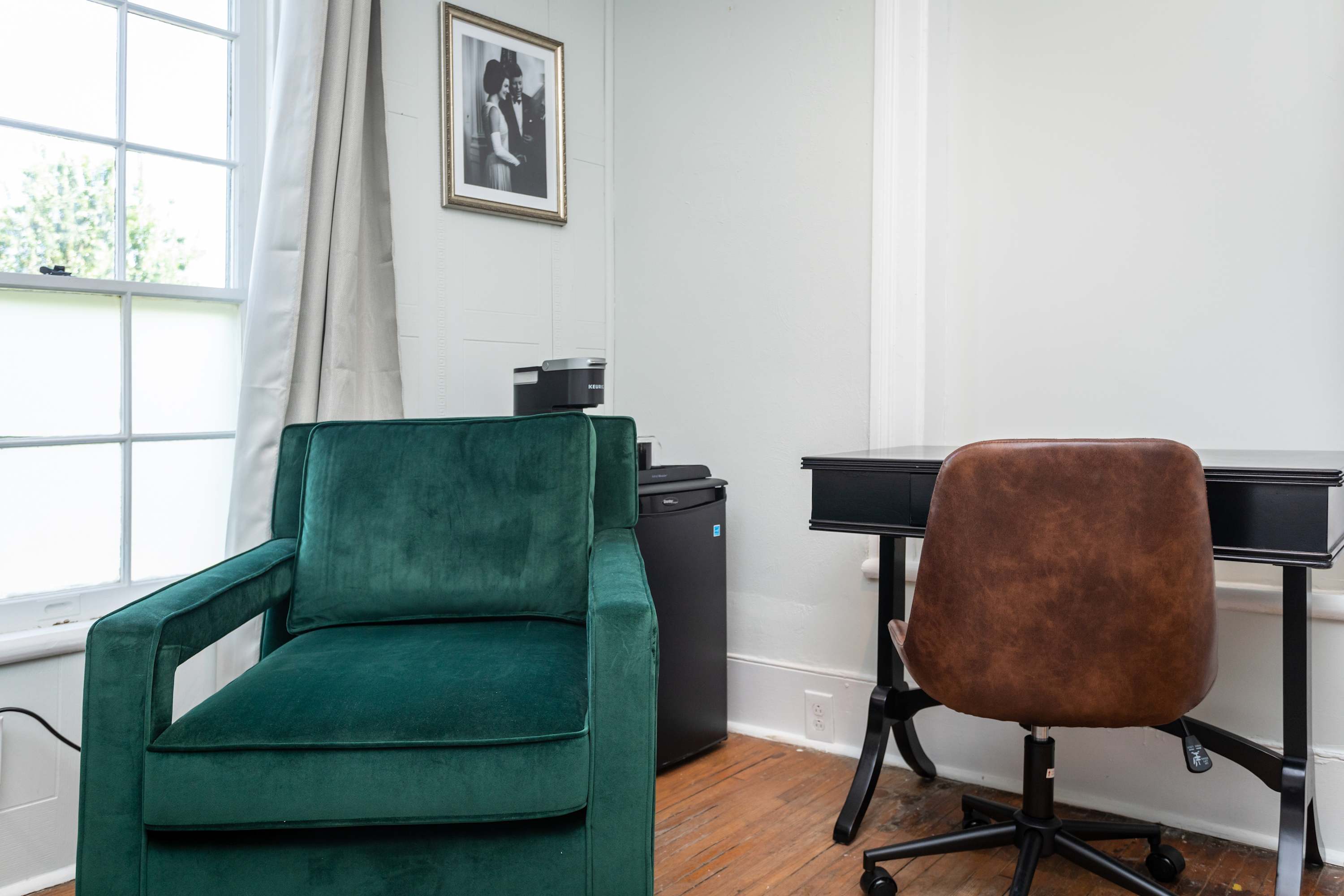 A cozy green armchair and a brown desk chair beside a window in a bright room.