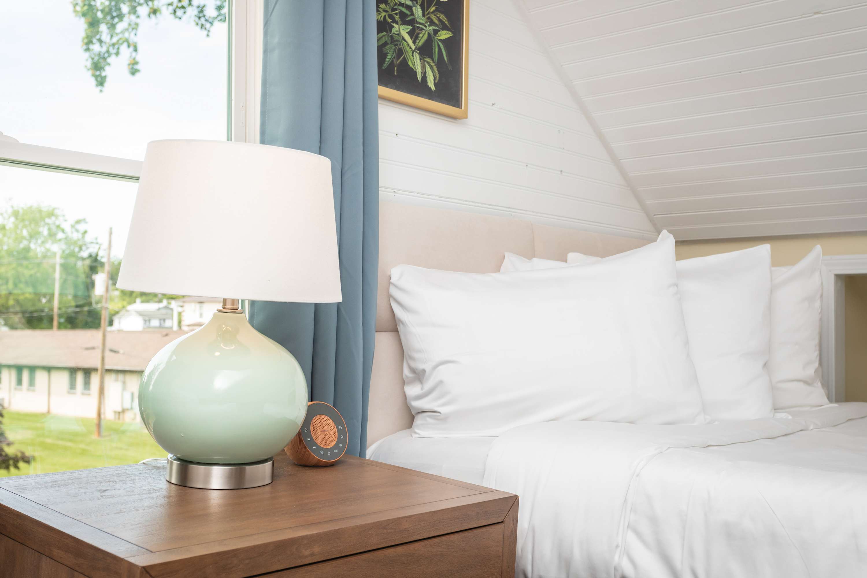A cozy bedroom corner featuring a soft bed with white linens and a bedside table with a ceramic lamp.