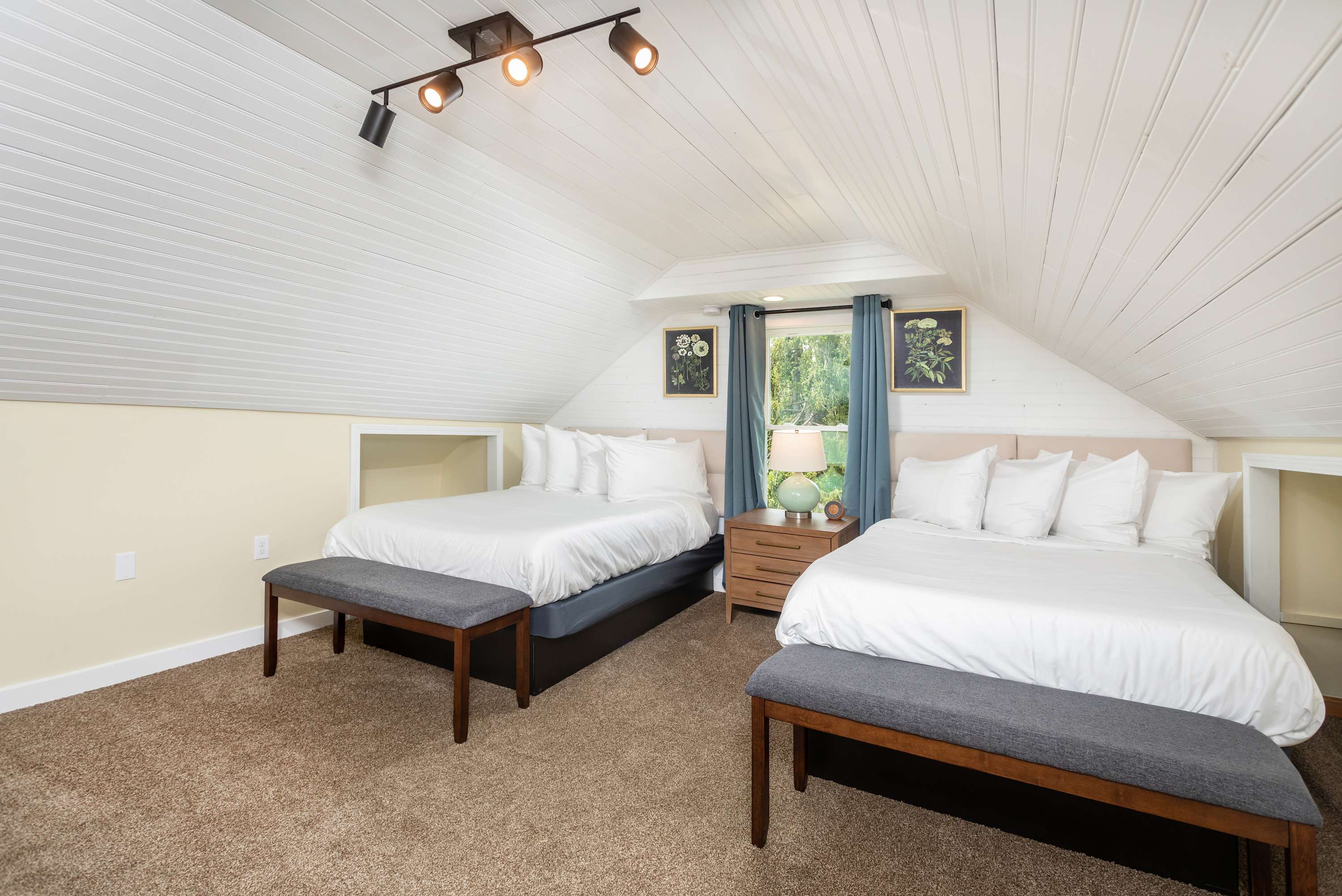 Two queen beds in a bright attic bedroom with white paneled ceilings and a window view.