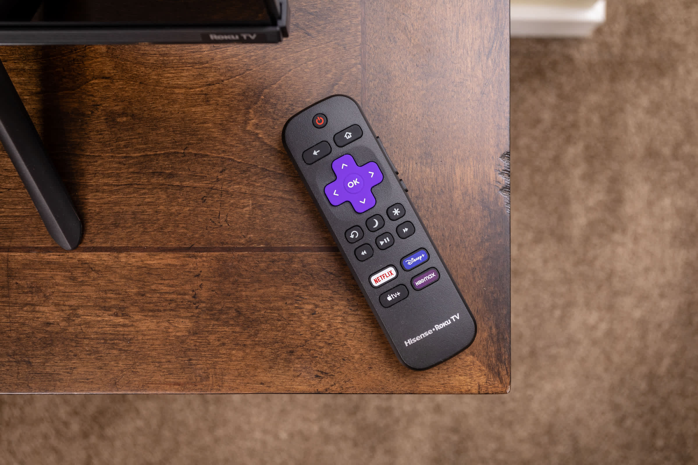 Remote control for streaming services on a wooden table next to a television.