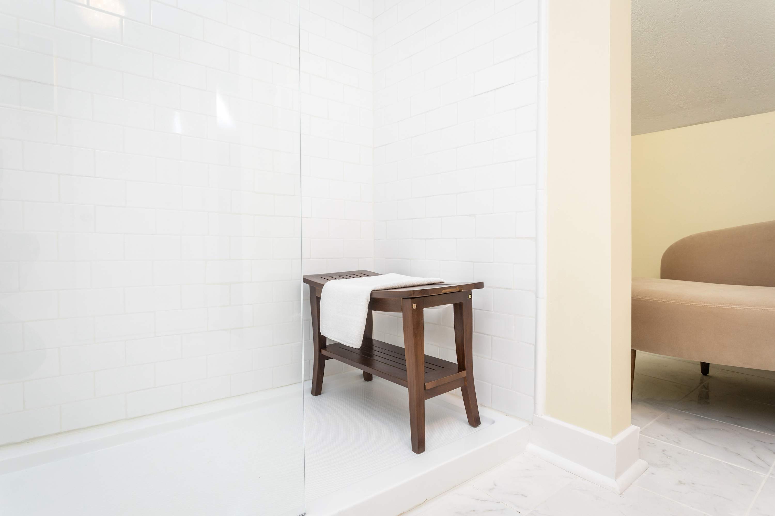 Modern walk-in shower with white subway tiles and a wooden bench.