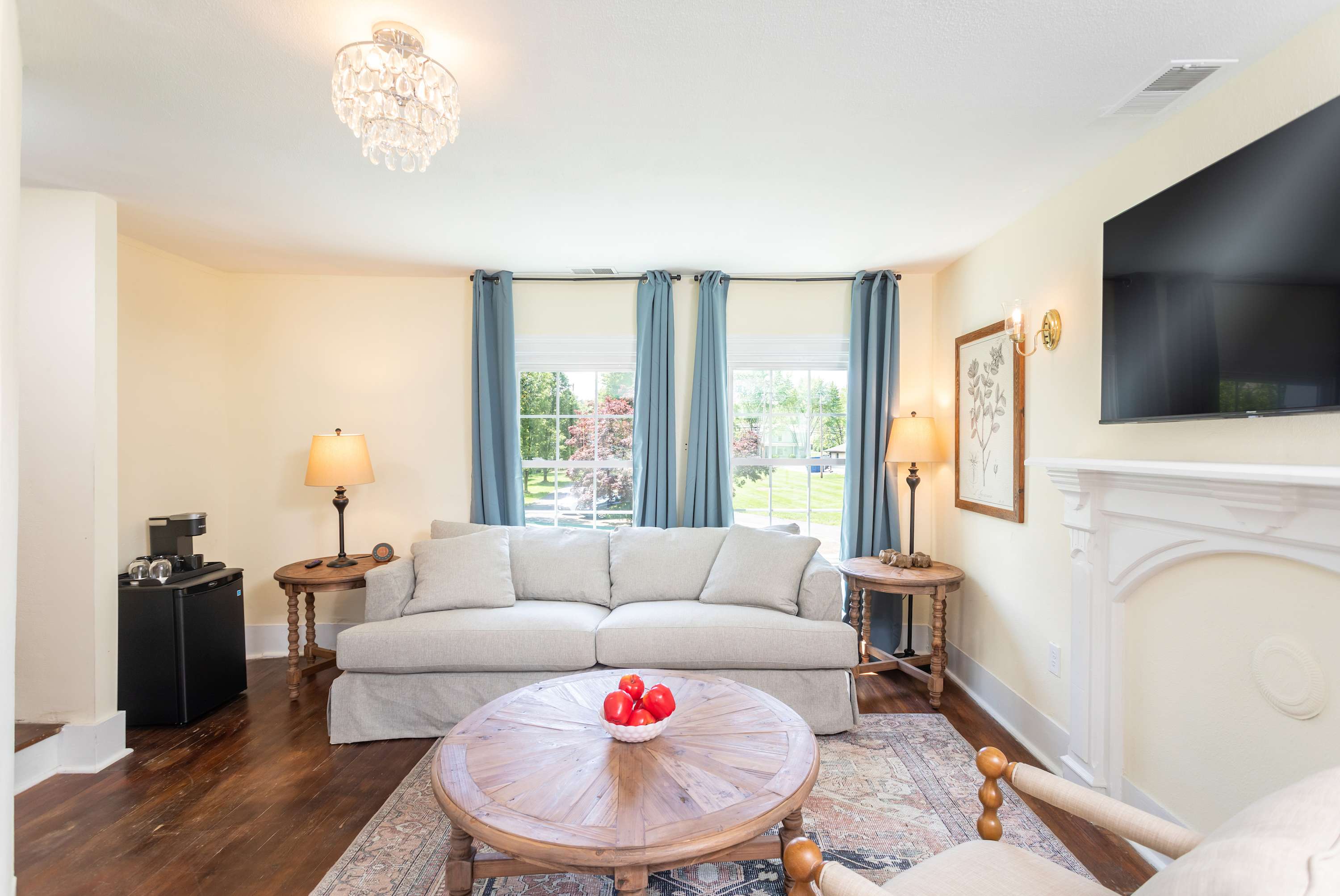 Relax in the bright living room featuring a comfortable sofa, wooden coffee table, and large windows with blue curtains.