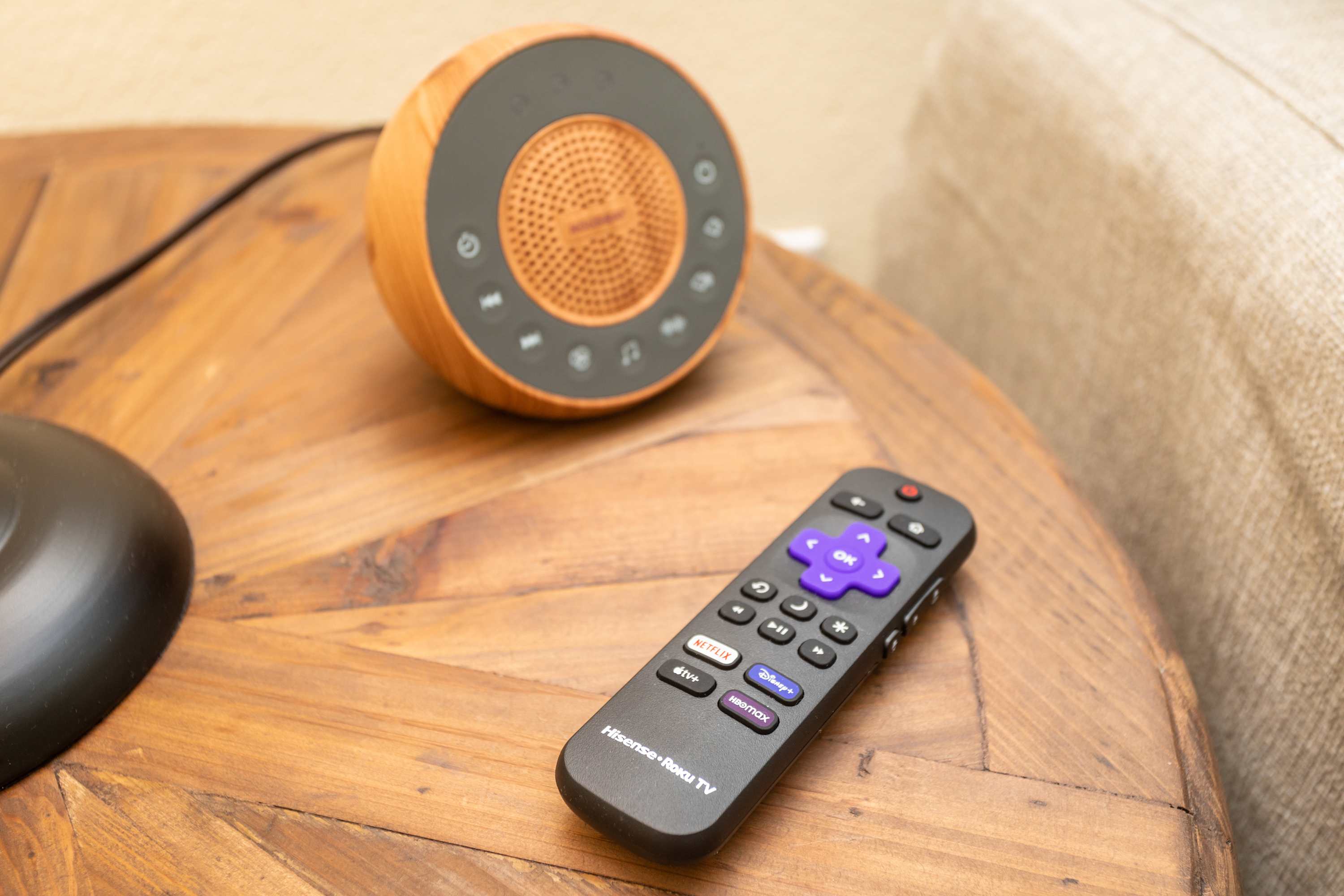 Remote control and speaker on a wooden side table next to the sofa