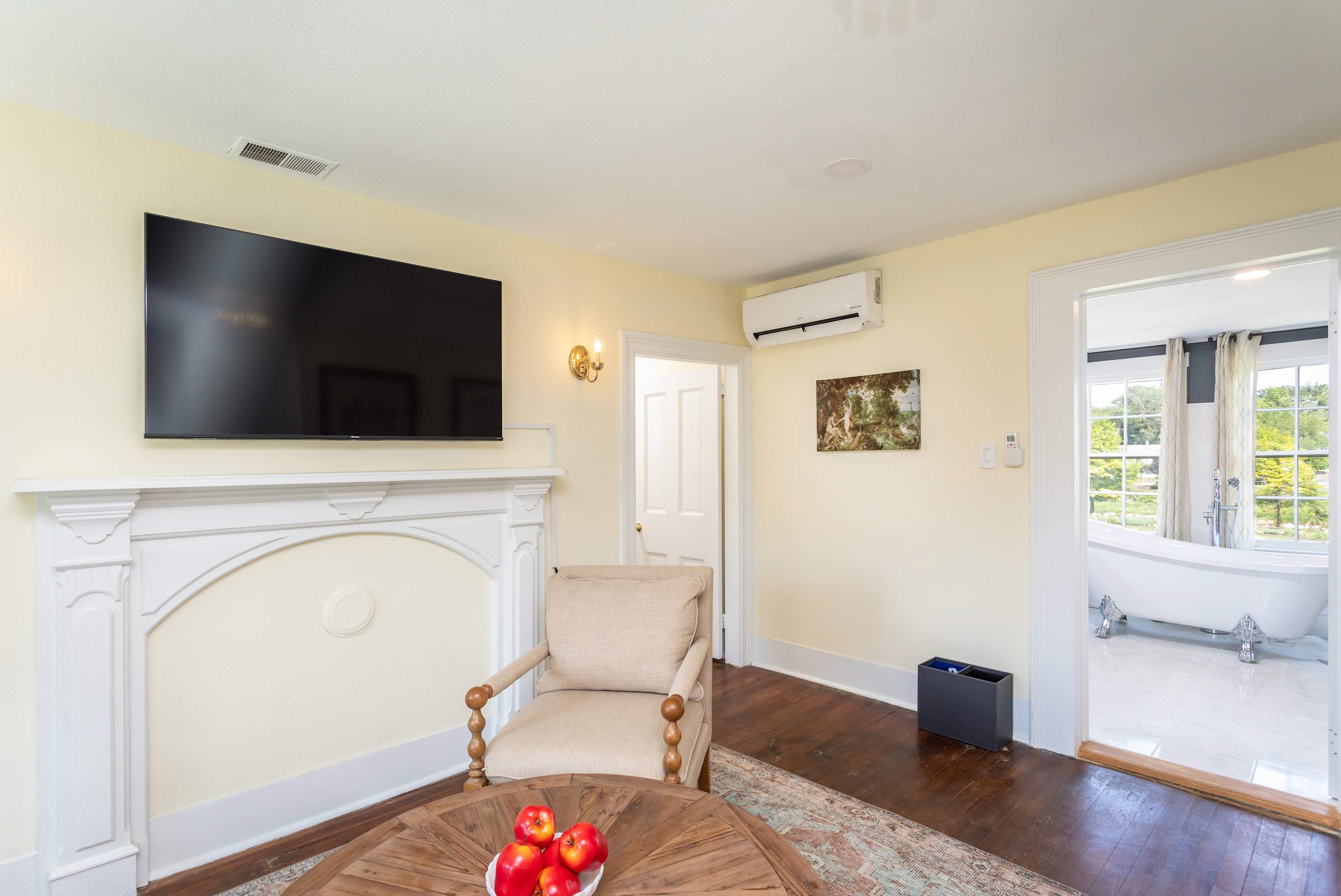 Living area with a mounted flat-screen tv and a view into the bathroom featuring a clawfoot tub.