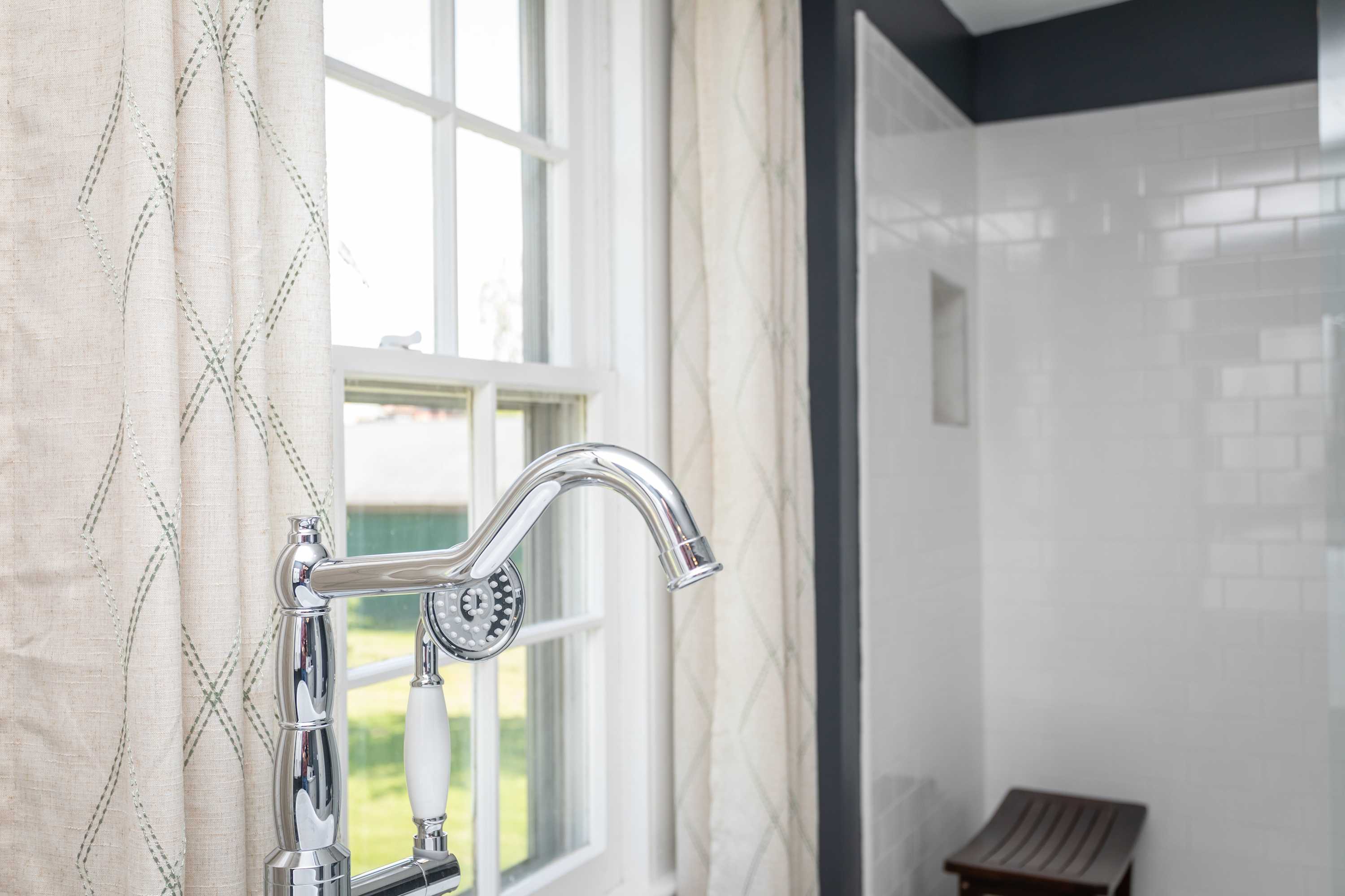 Modern bathroom faucet with a handheld showerhead next to a window with patterned curtains.