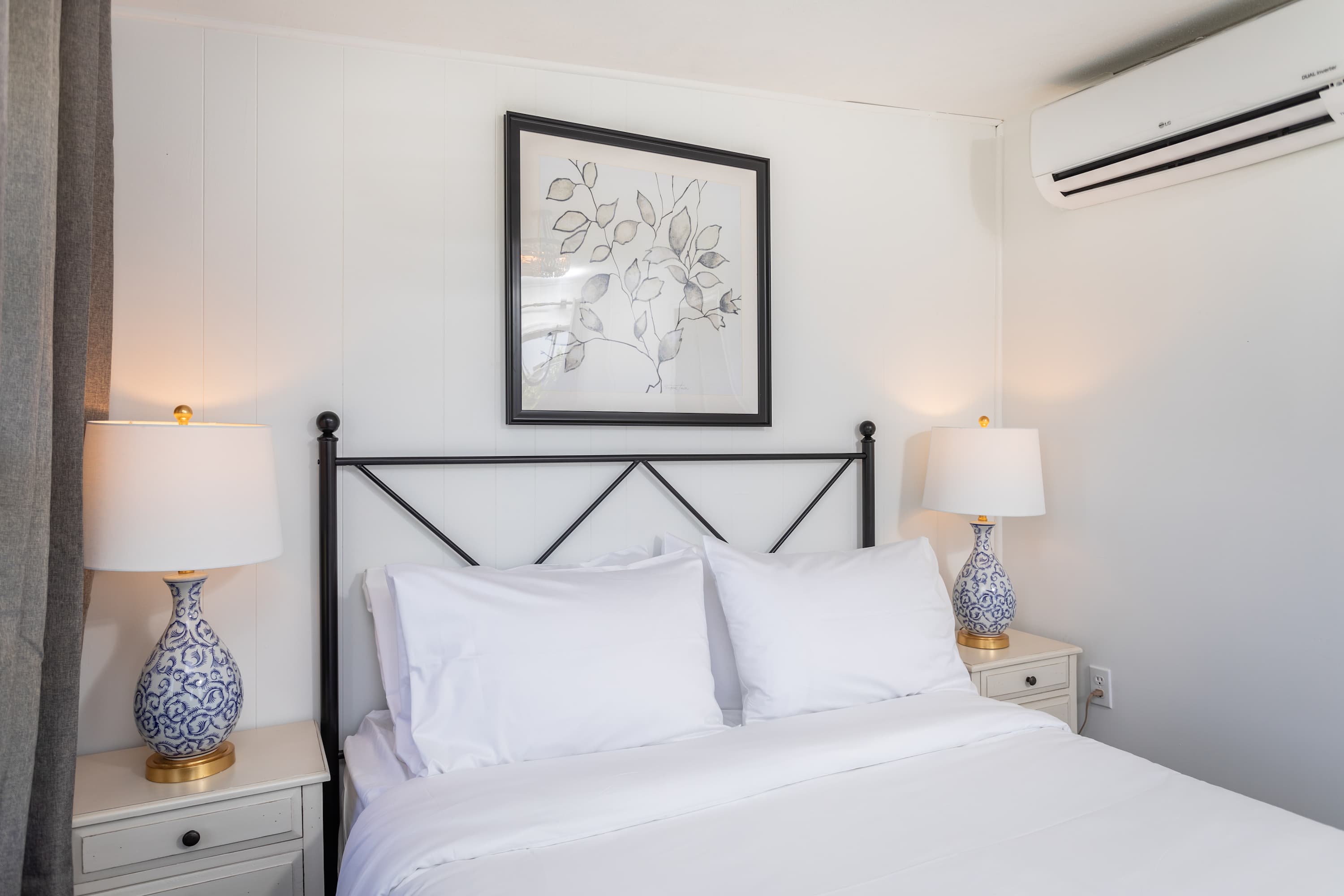 A cozy bedroom featuring a metal bed frame, white linens, and matching bedside lamps with blue patterned bases.