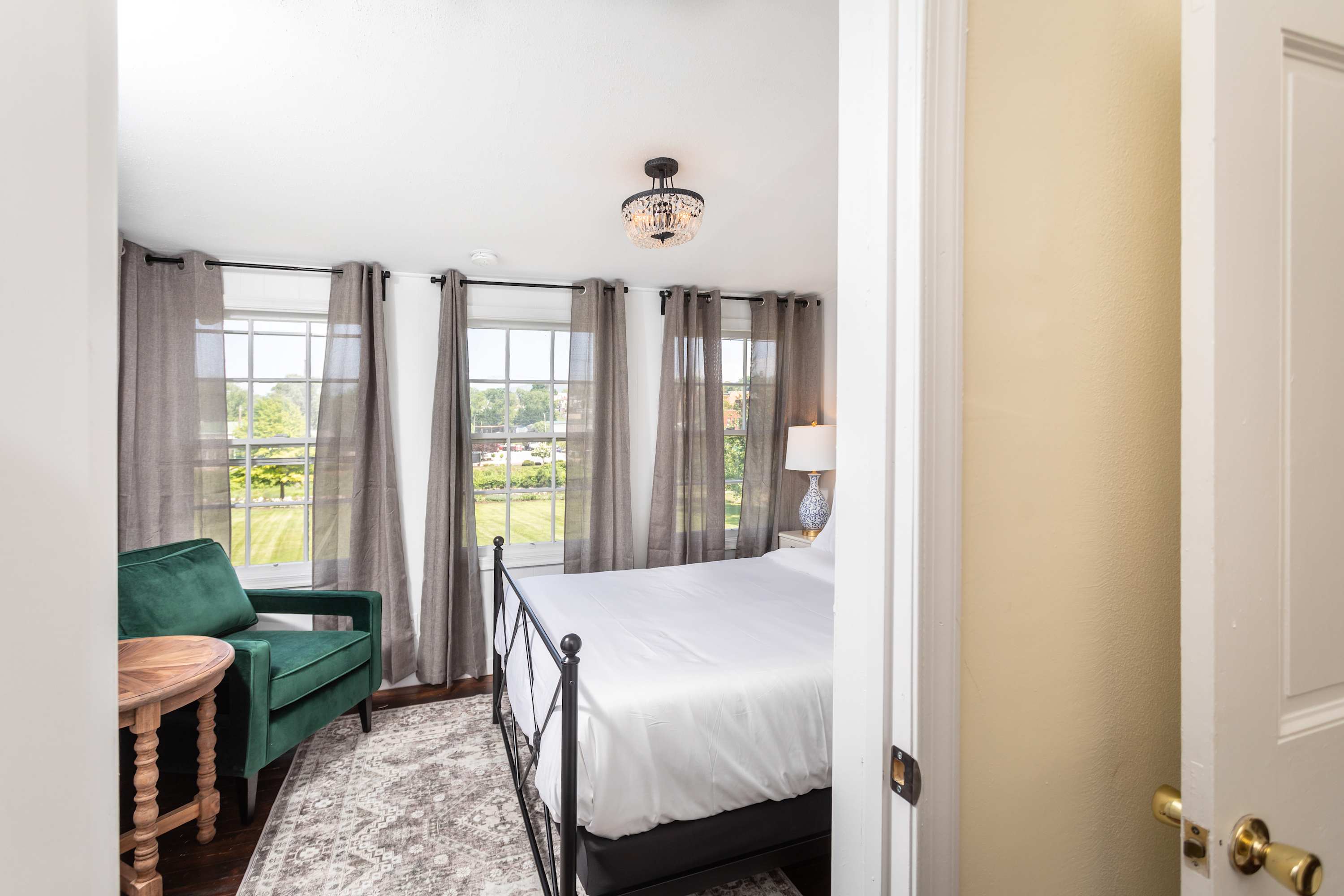 Bright bedroom with large windows, sheer curtains, and a green armchair for relaxing.