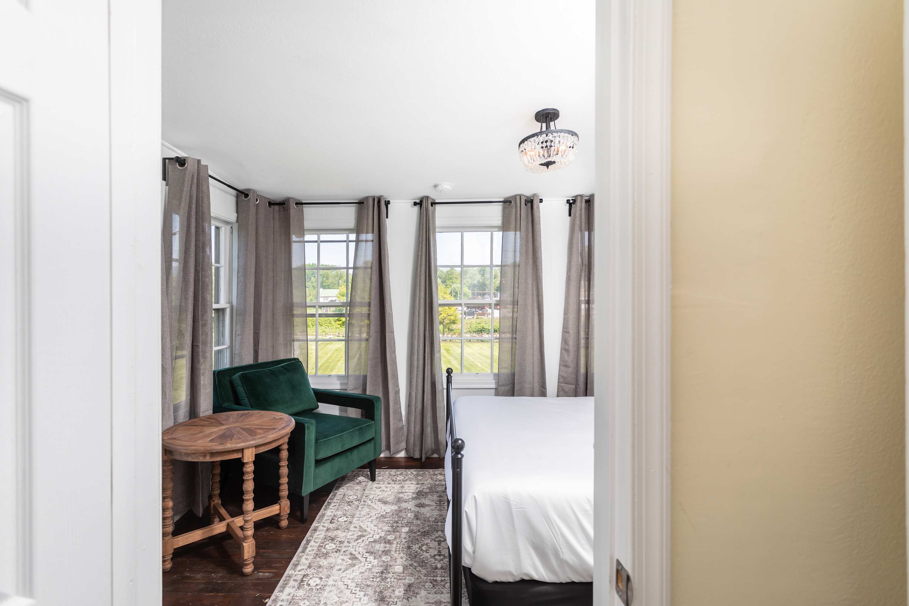 Cozy bedroom with large windows, a green armchair, and a rustic wooden side table.
