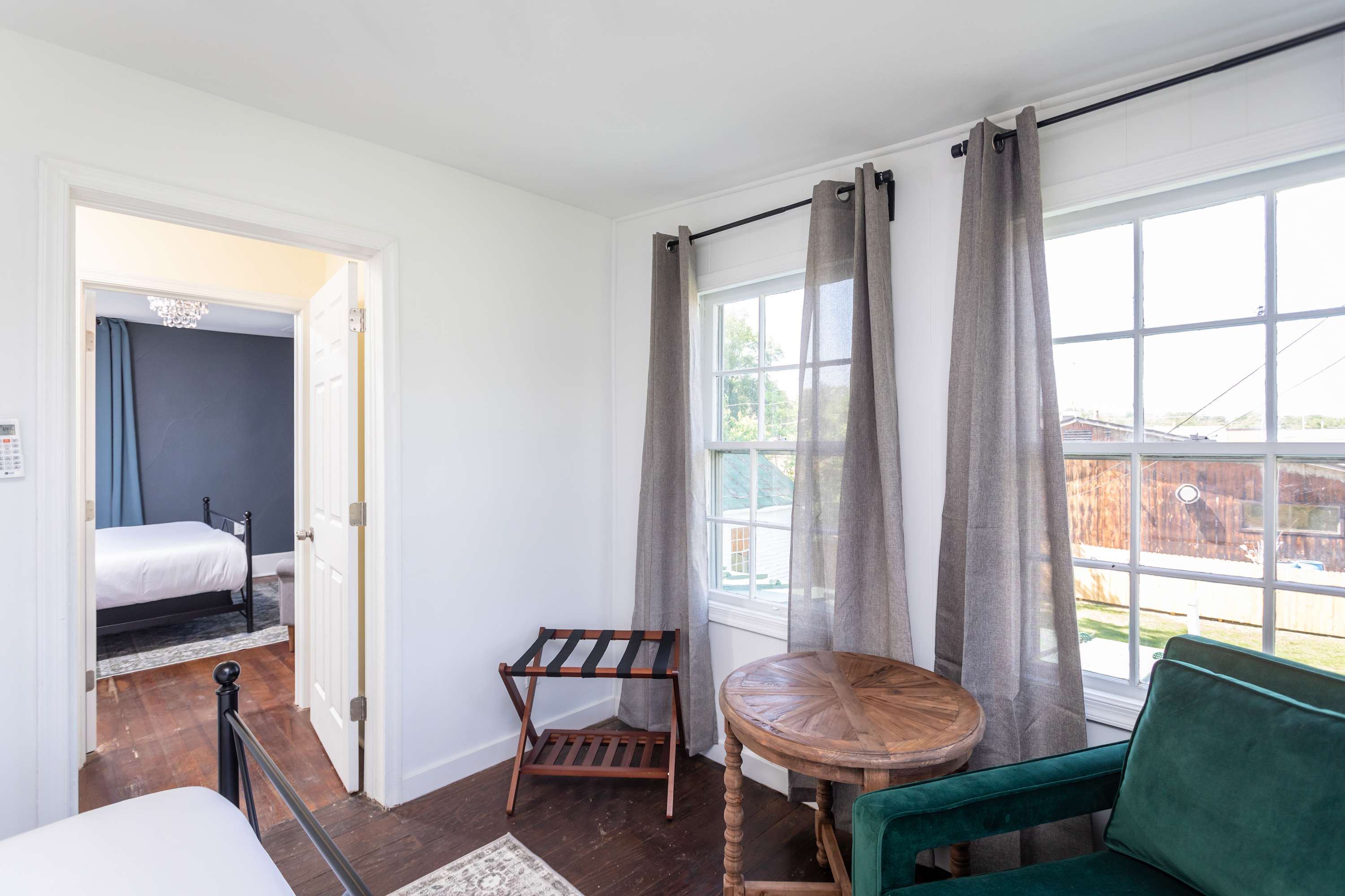 Natural light fills this cozy sitting area with a green armchair and wooden table next to large windows.