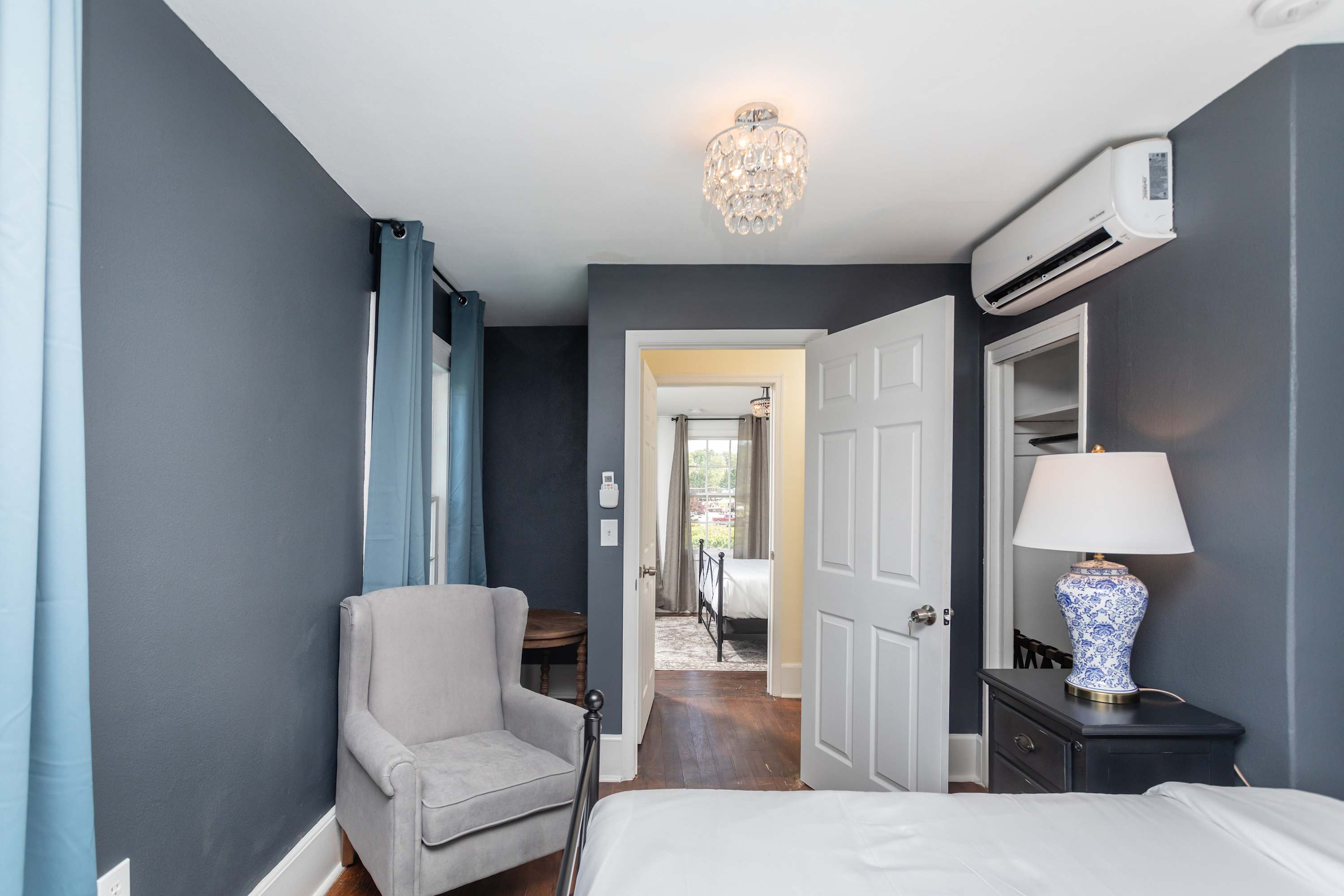 Cozy bedroom with a gray armchair, blue curtains, and a decorative lamp on a black nightstand.