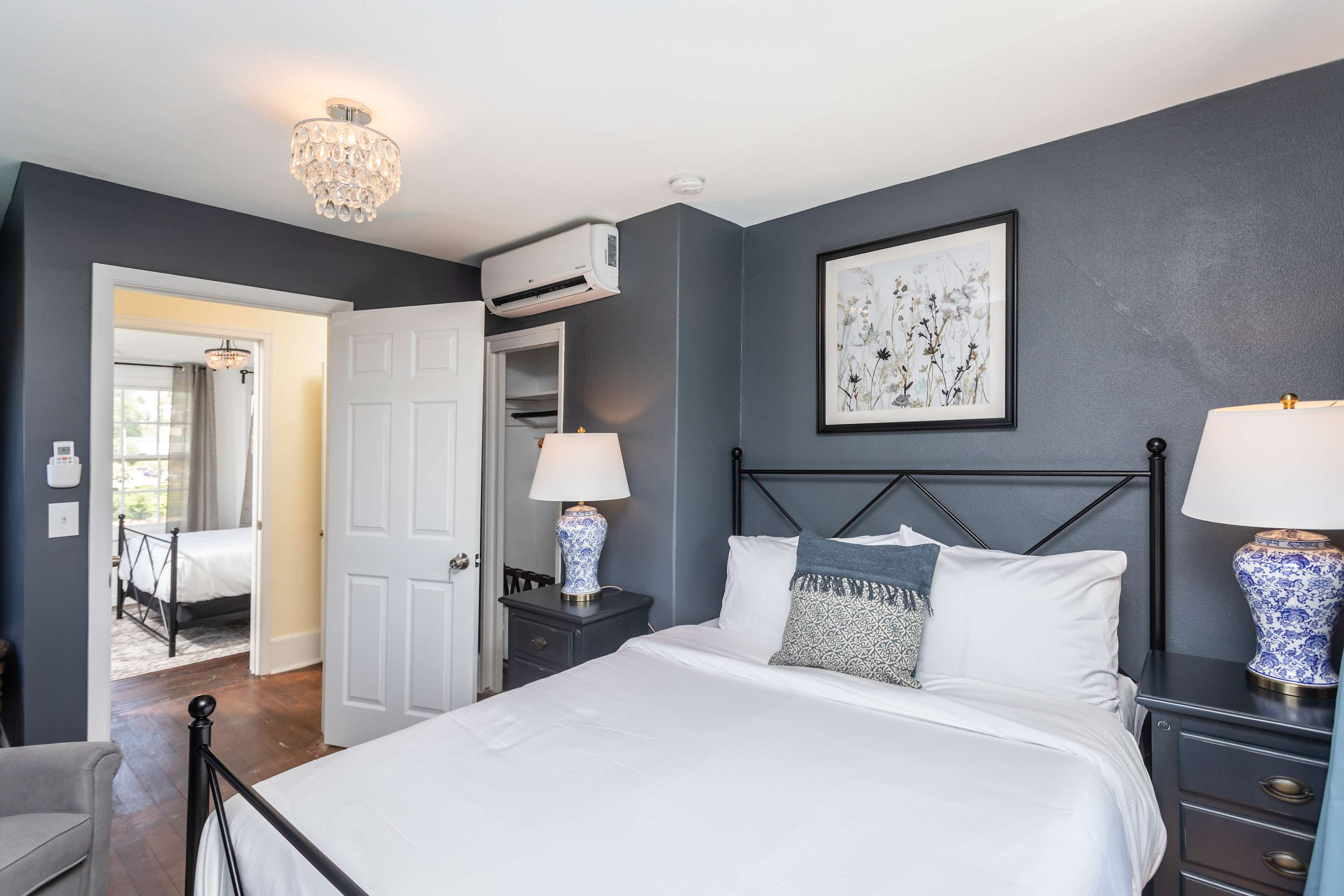 Cozy bedroom with dark gray walls, decorative lamps, and a view into the adjacent room.