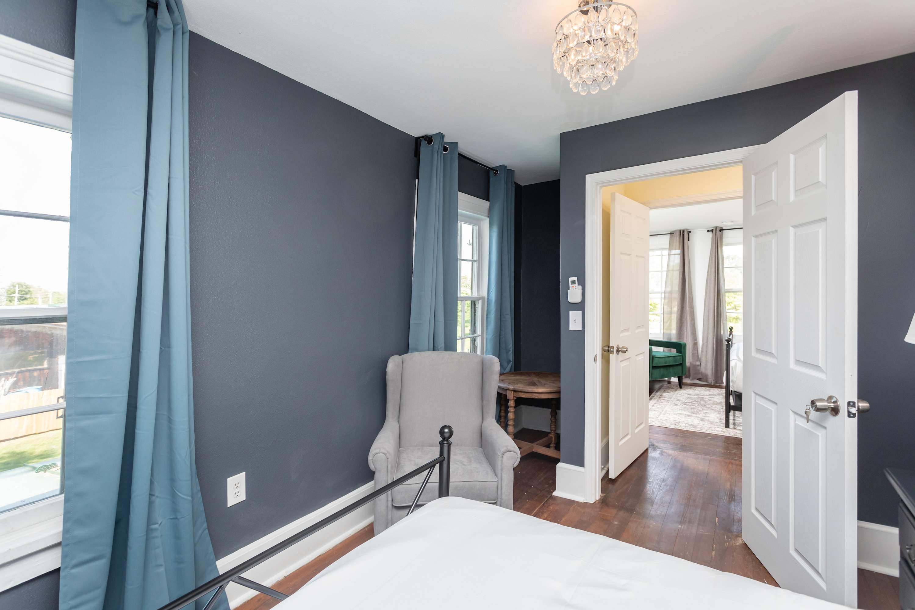 Cozy bedroom corner with a gray armchair and natural light from two windows.