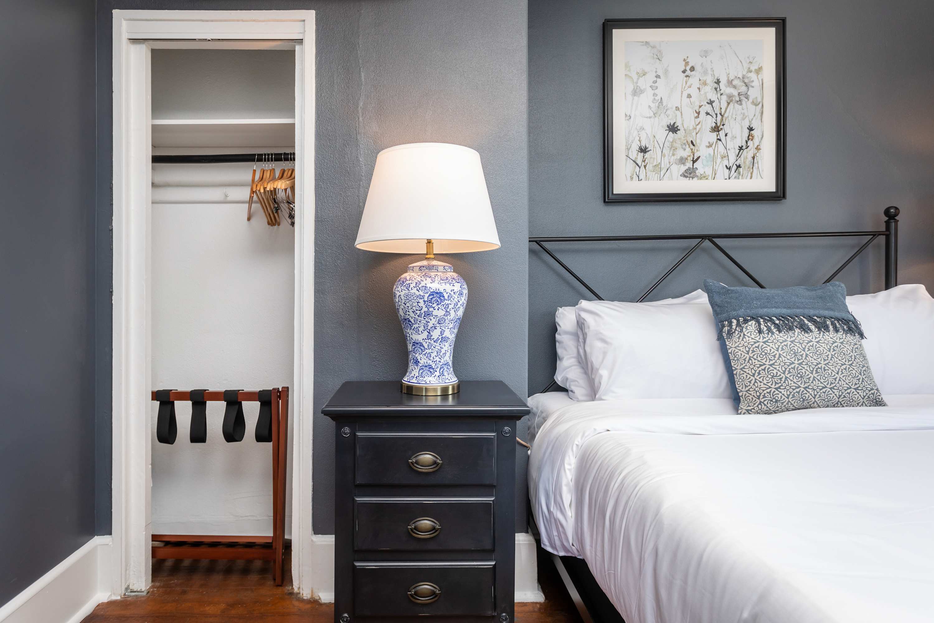 A cozy bedroom corner featuring a black nightstand with a decorative lamp and an open closet with hangers.