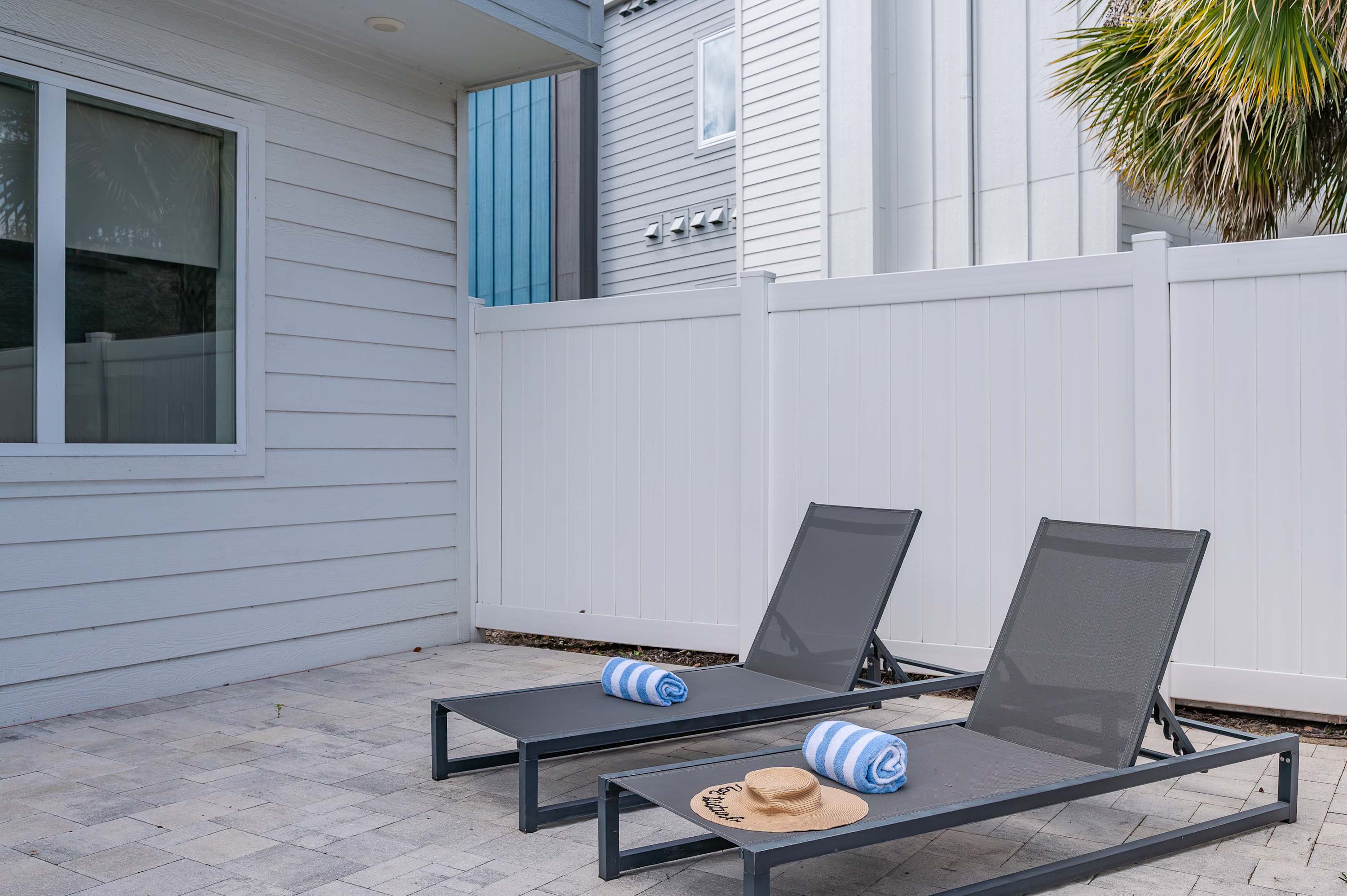 Two modern lounge chairs with towels and a sun hat on a private patio area.