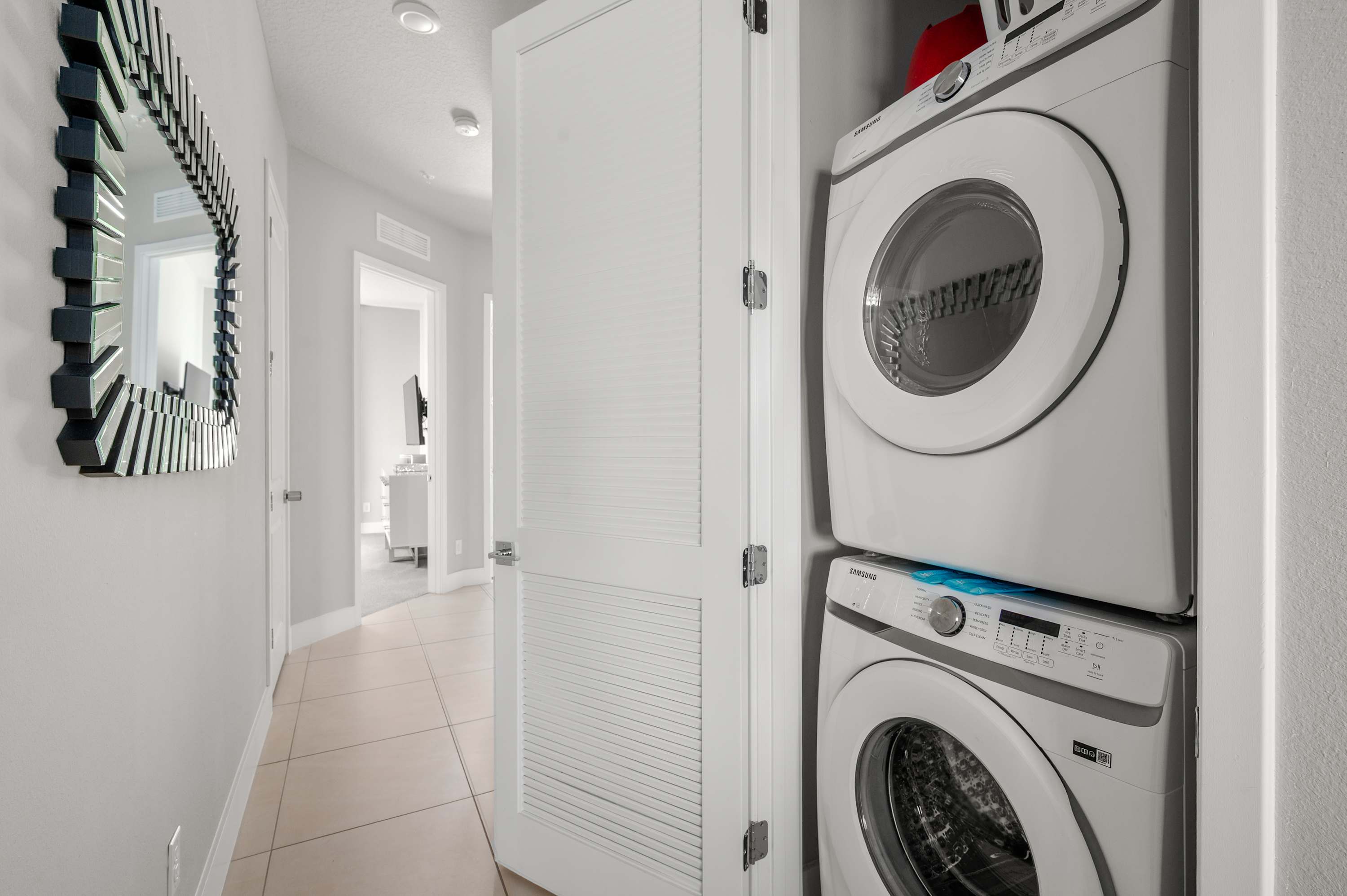 Stacked washer and dryer in a compact laundry closet with a decorative mirror in the hallway