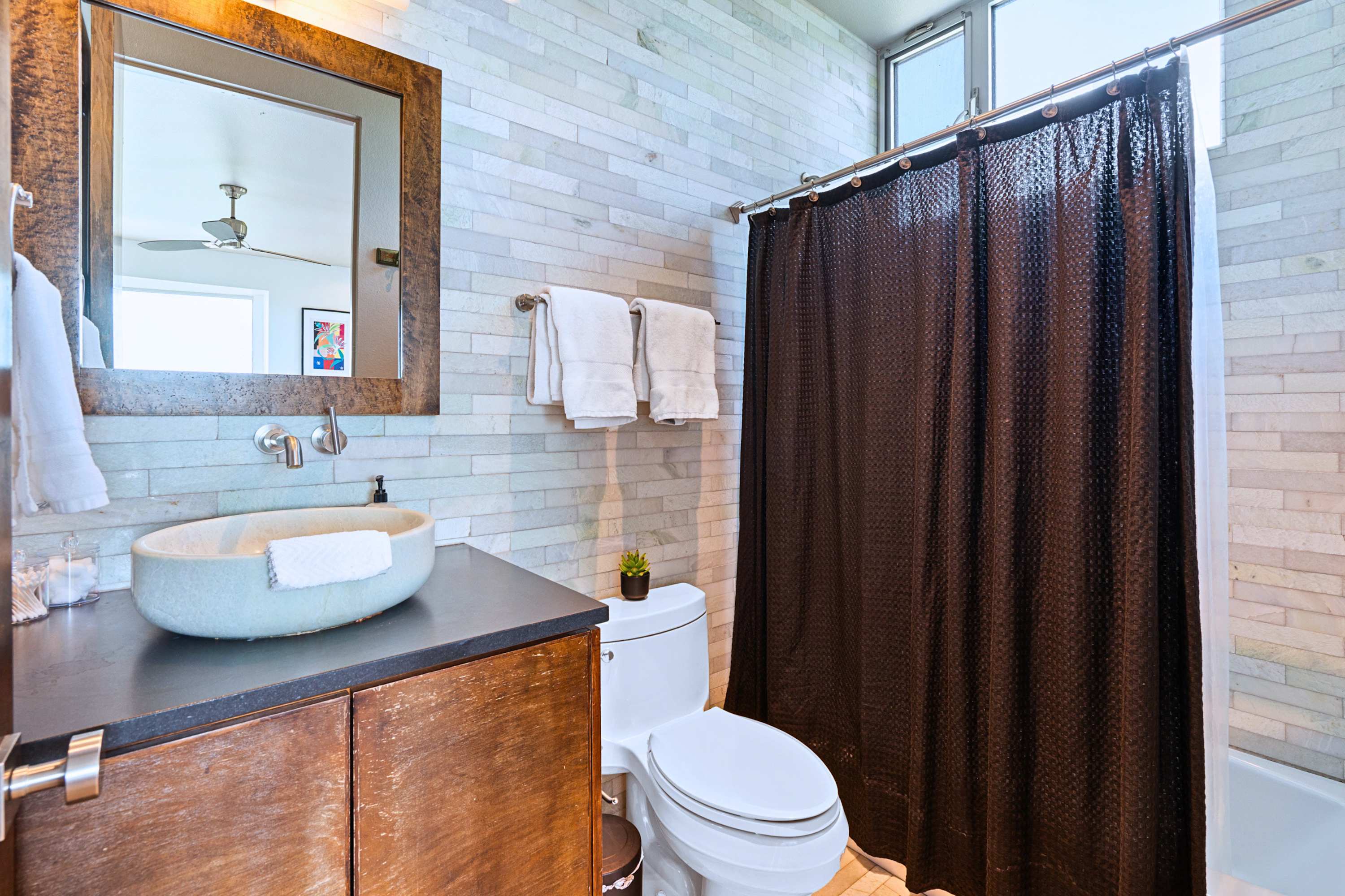 Main: Sleek stone-tiled walls and a pristine vanity create a clean, refreshing space.