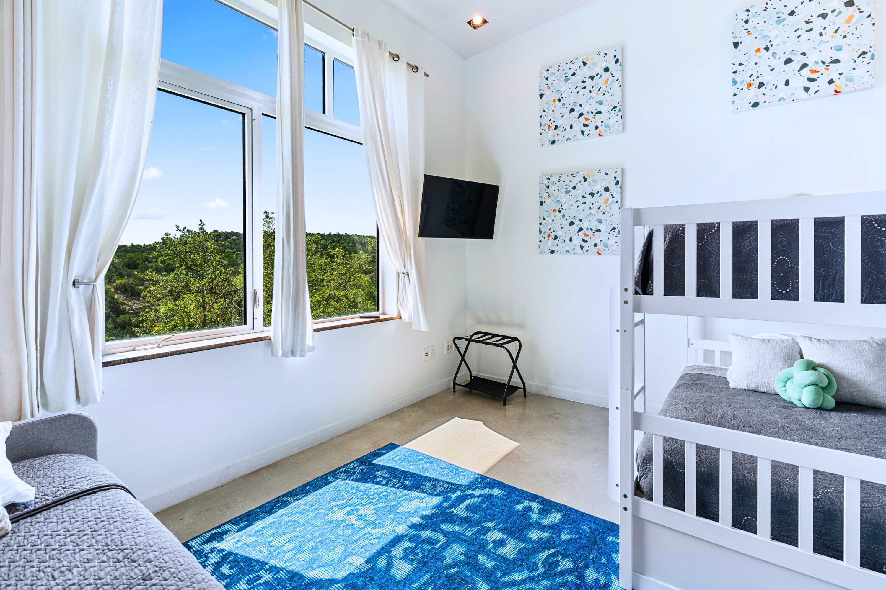 Main: Bright, playful bunk room featuring scenic tree-canopy views and plush bedding.