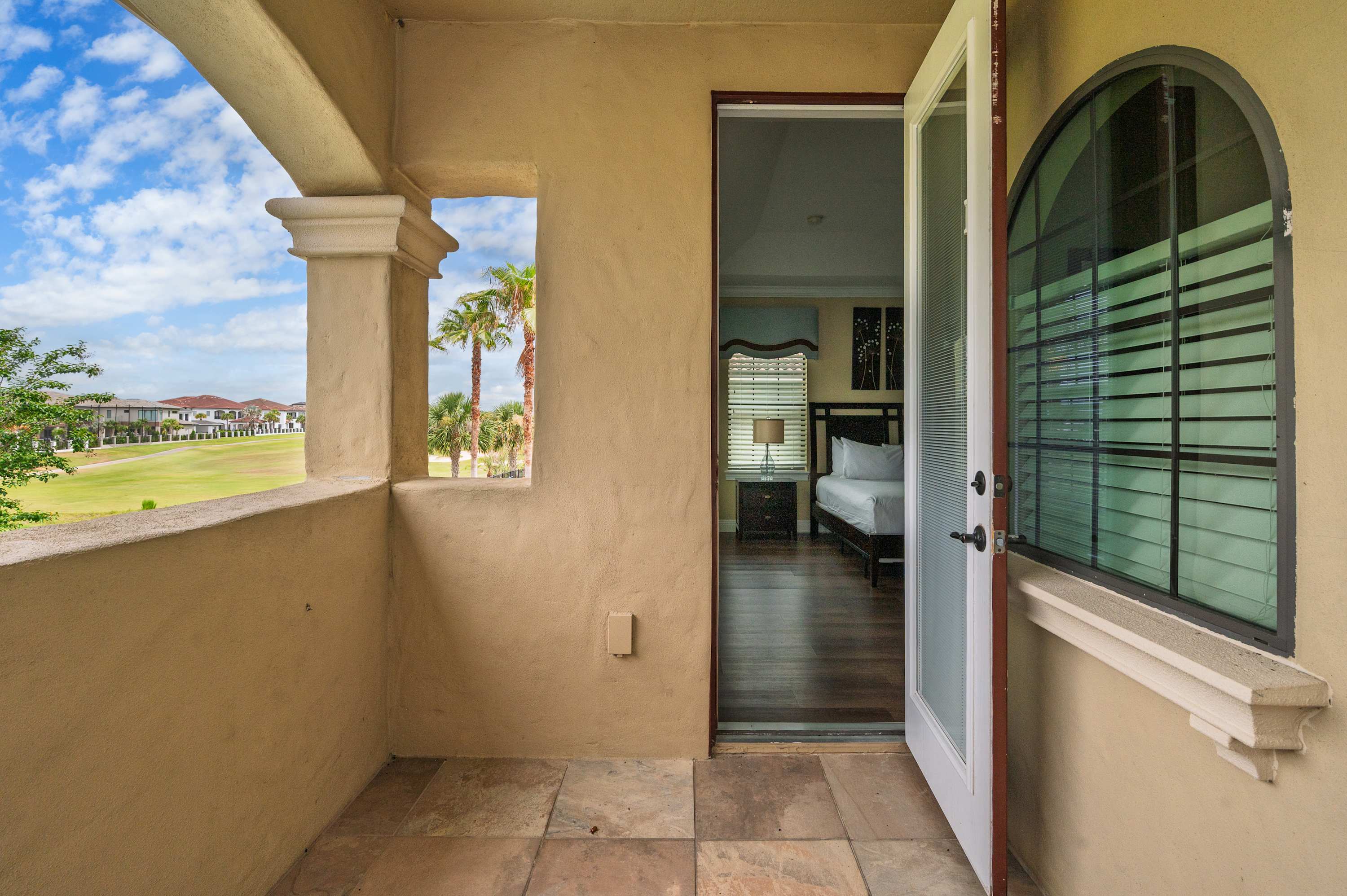 Covered balcony with views of a golf course and palm trees