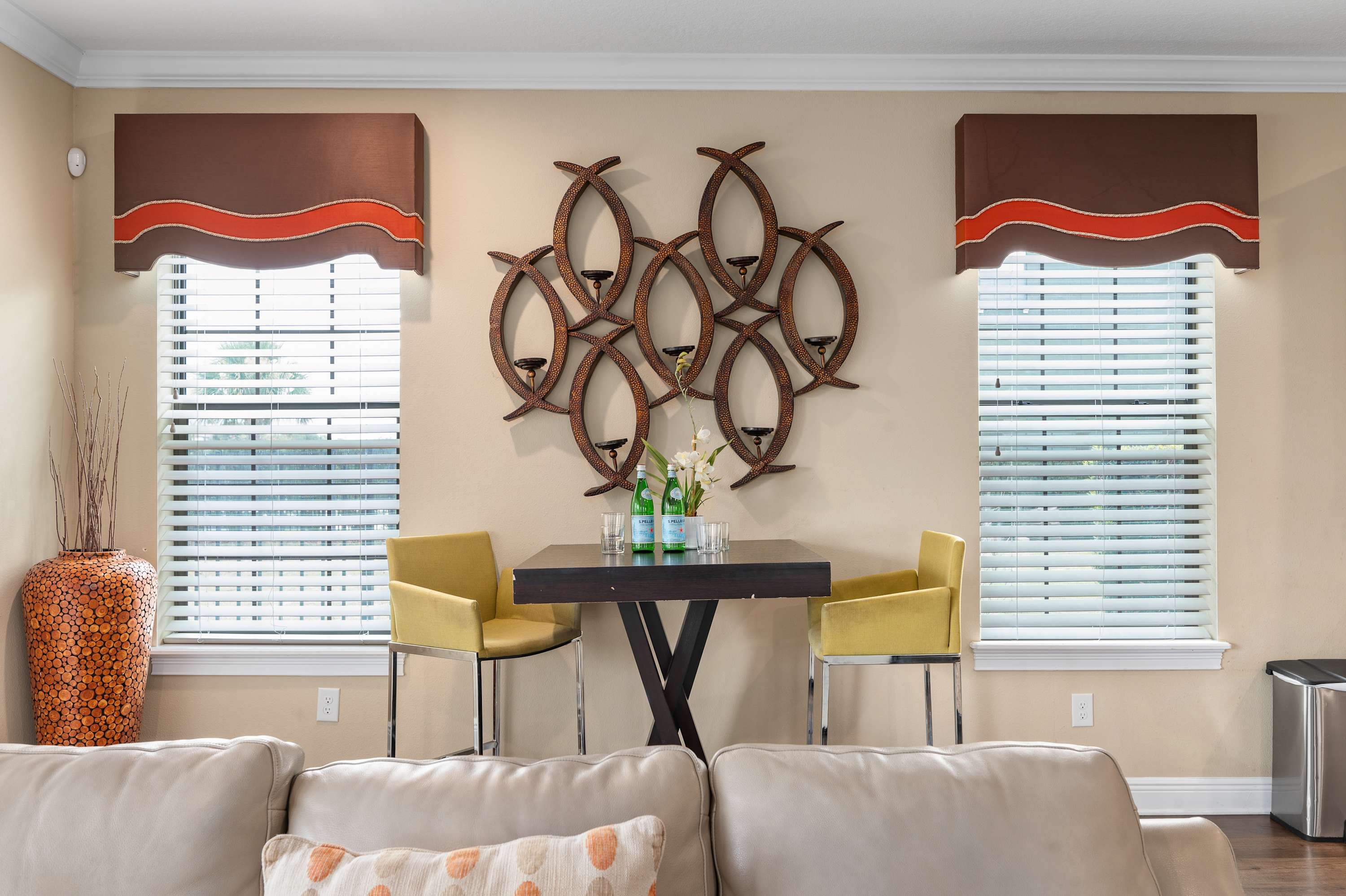 Dining area with modern yellow chairs and decorative wall art between two windows.