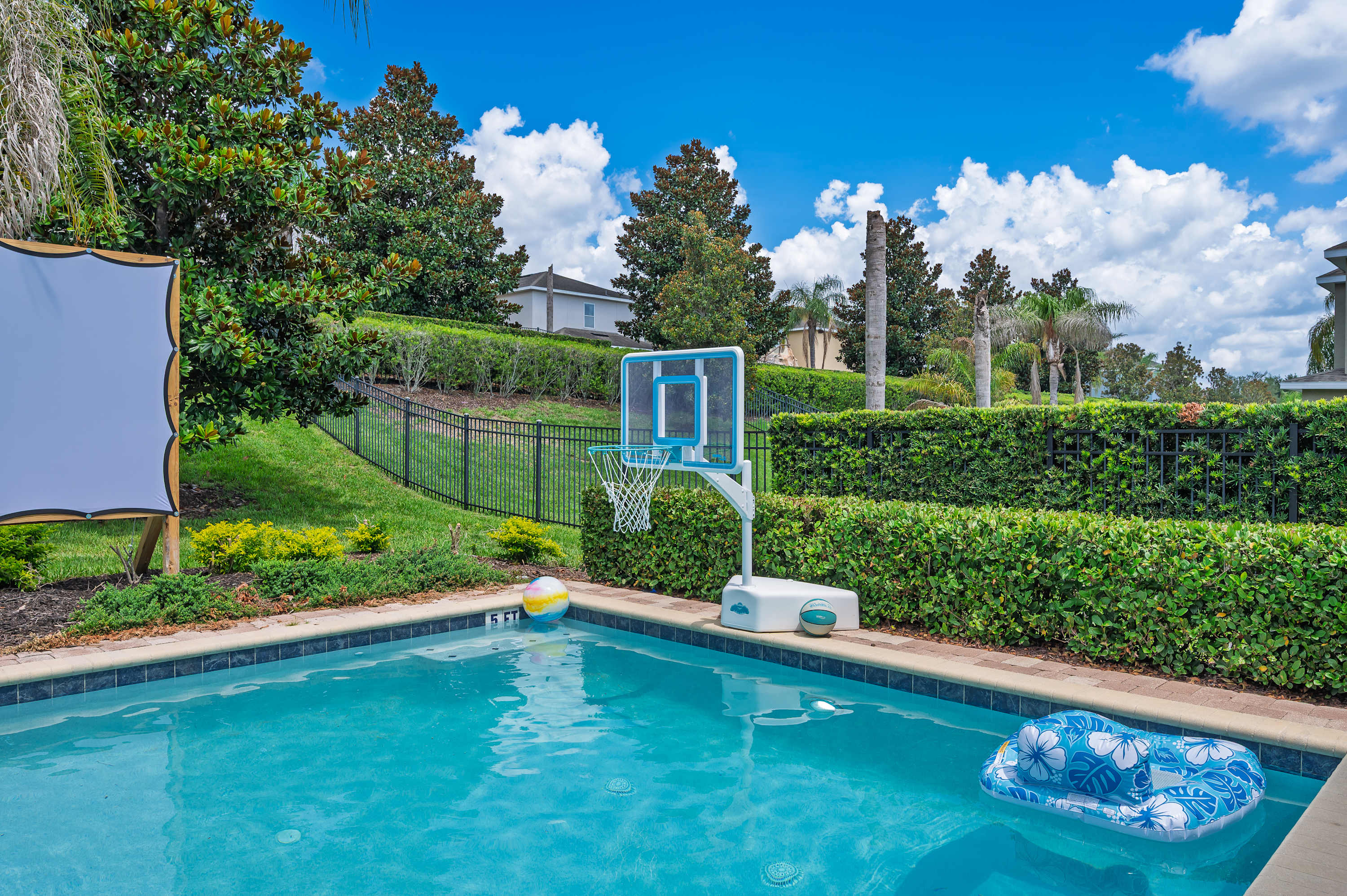 Outdoor pool area with a basketball hoop and inflatable float under a clear blue sky