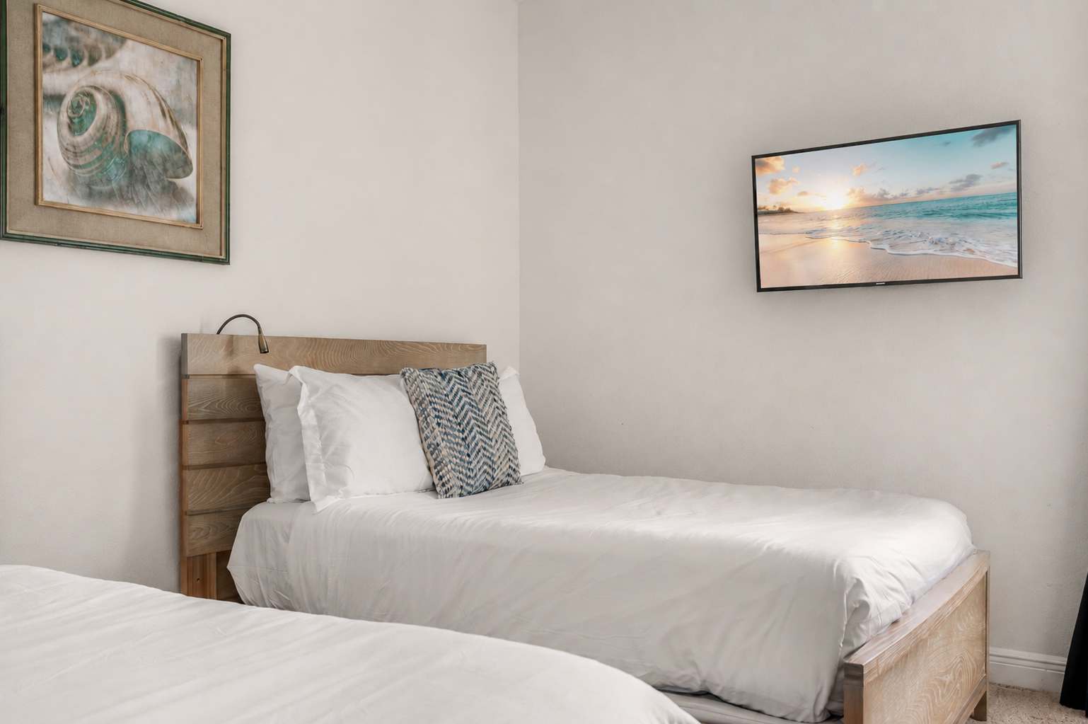 Simple bedroom with twin beds, a wall-mounted television, and coastal artwork.