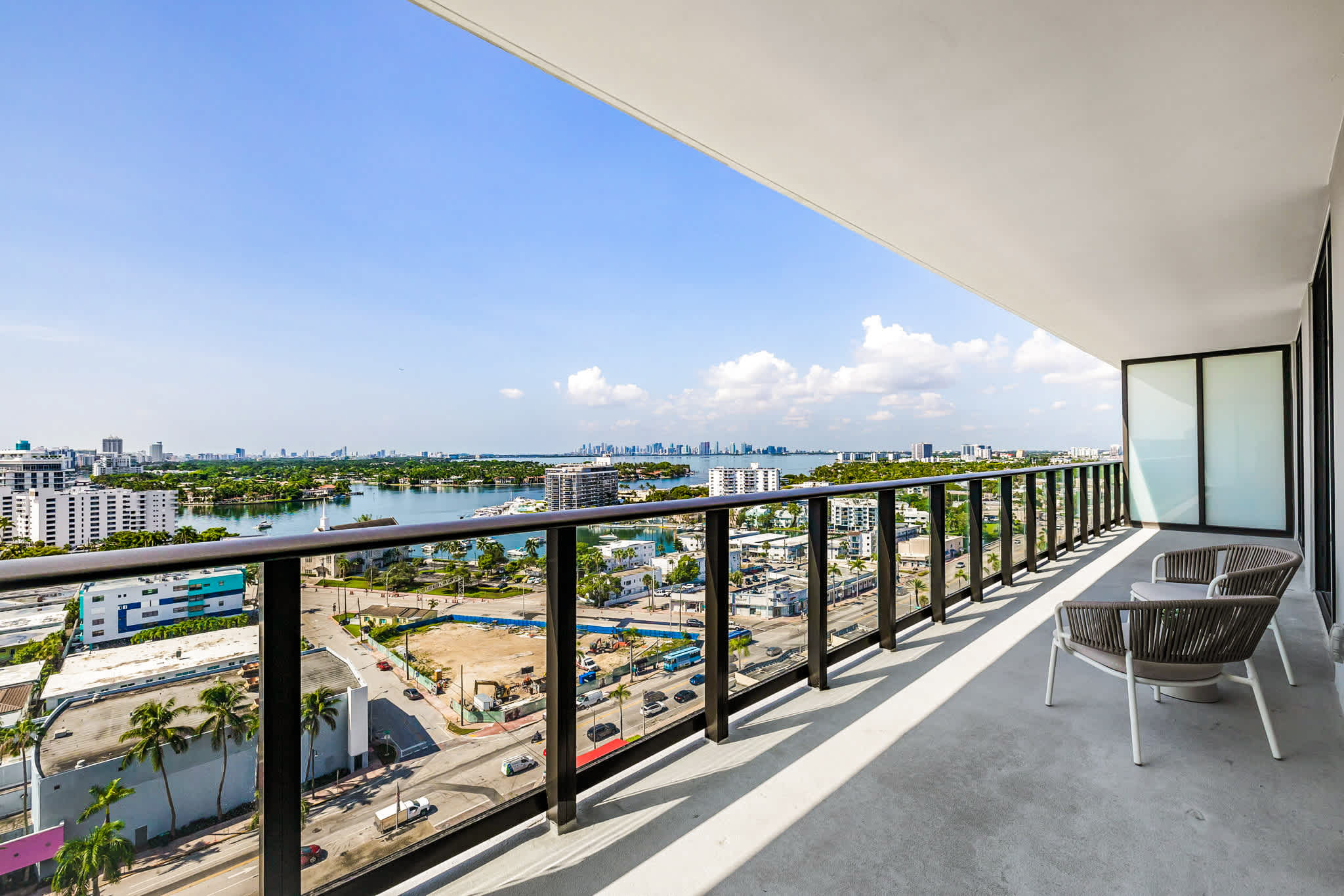 Private balcony with two lounge chairs and sweeping water, marina, palm-tree, and skyline views.