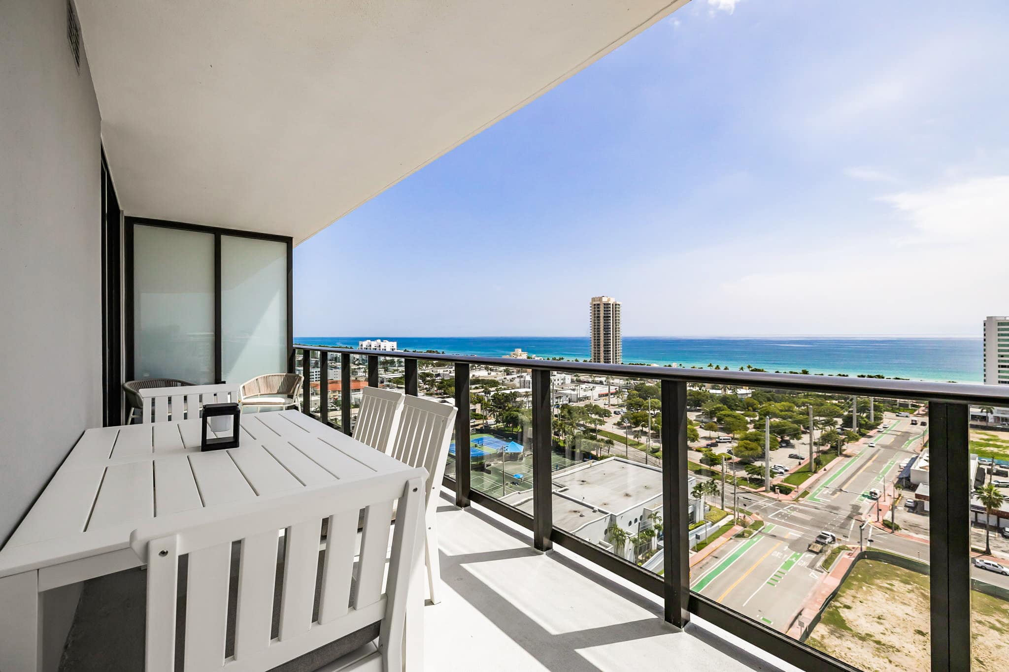 Private balcony dining with sweeping ocean views, a turquoise shoreline, and the coastal city skyline beyond.