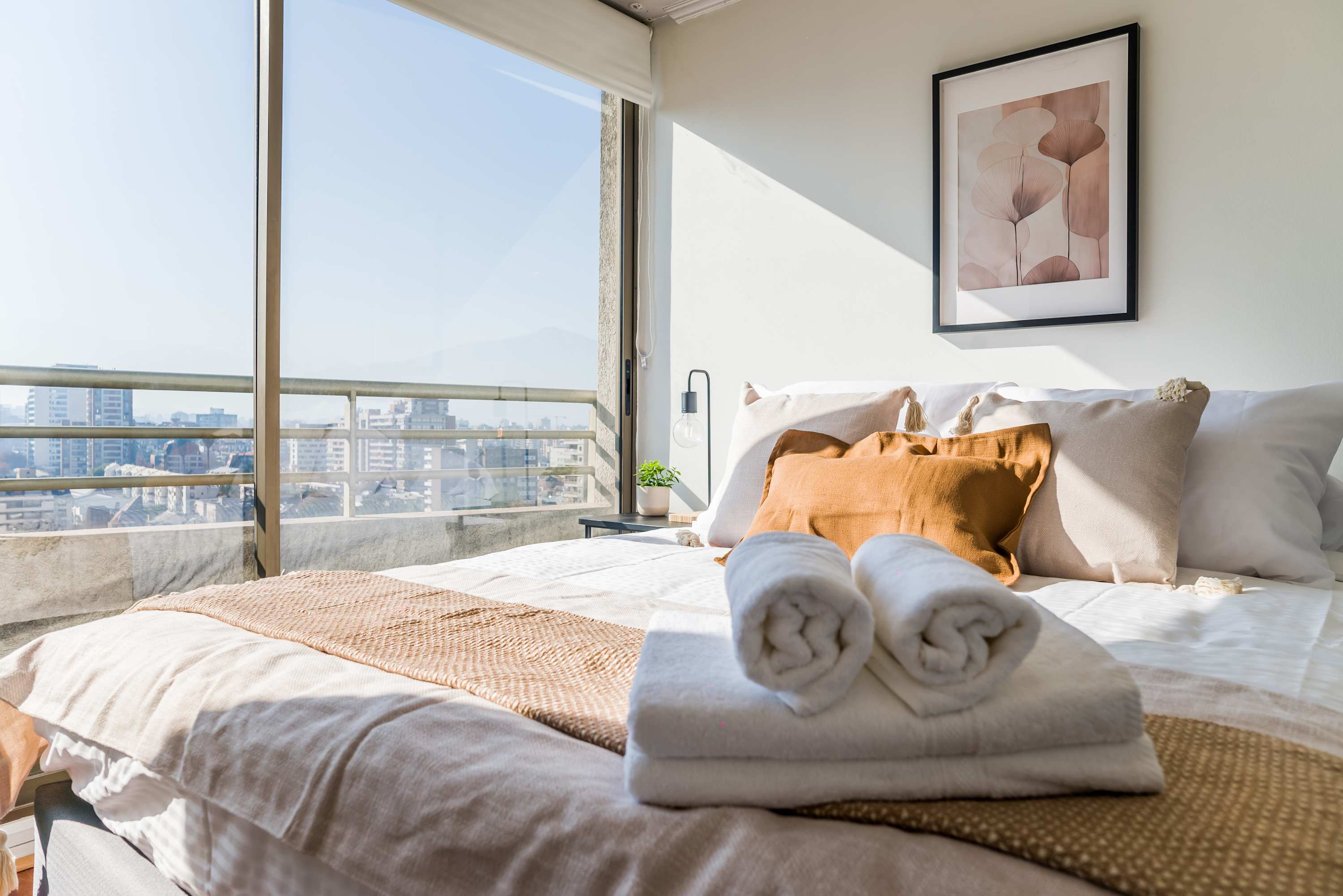 Relax in a sunlit bedroom with stunning city views and plush bedding, perfect for unwinding after a day of exploring Santiago.
