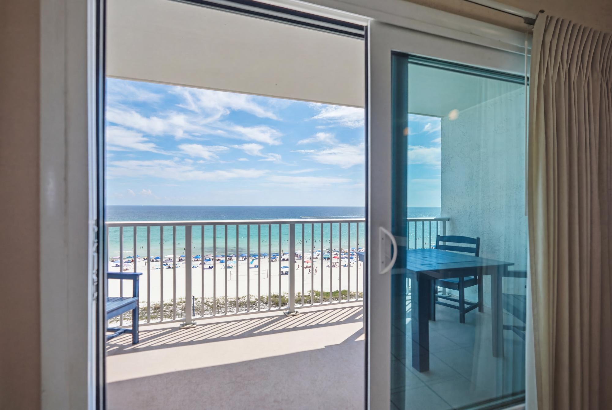 The Summit 830 – View from balcony showing beach, ocean, and sunlight with a table and chairs.