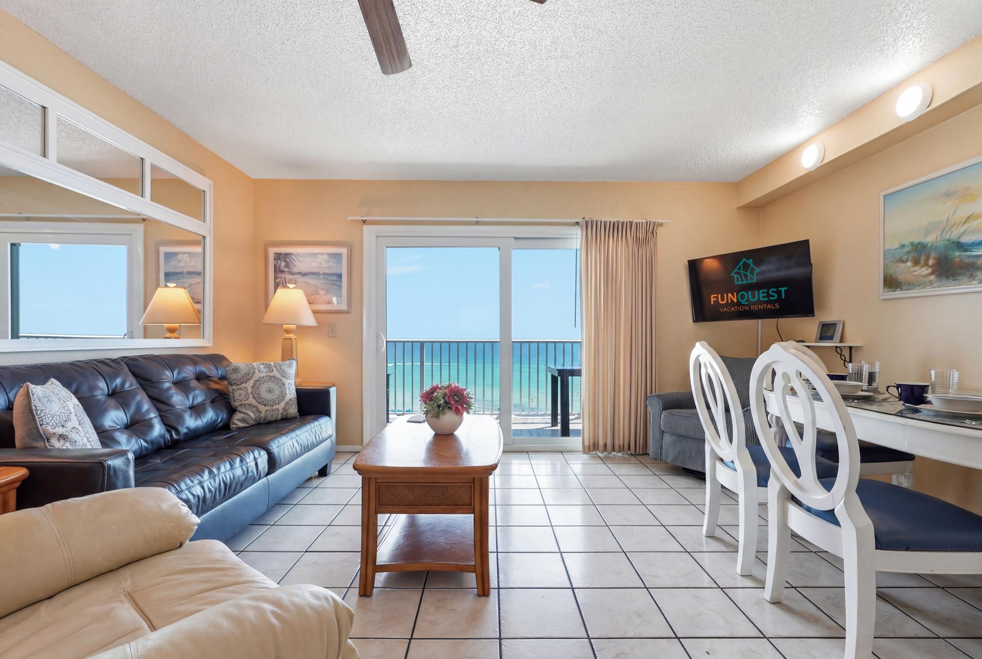 The Summit 830 – Living room with ocean view, leather sofa, dining table, and wall-mounted TV.