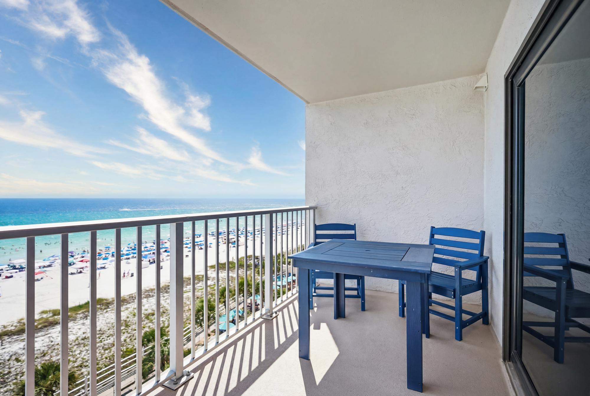 The Summit 830 – Balcony view overlooking beach with blue chairs and table, clear sky and ocean in the background.