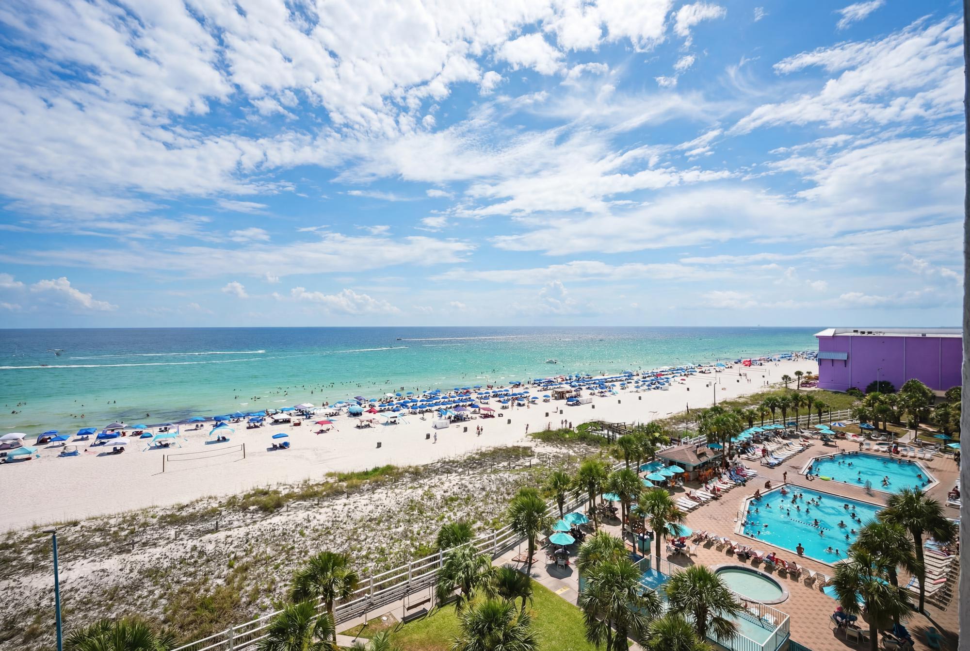 The Summit 830 – View of beach, umbrellas, turquoise ocean, and two swimming pools from a height.
