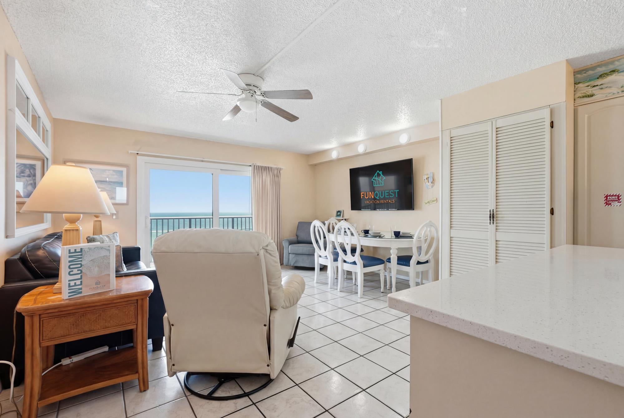 The Summit 830 – Living room with a view of the ocean, dining table, white furniture, and ceiling fan.