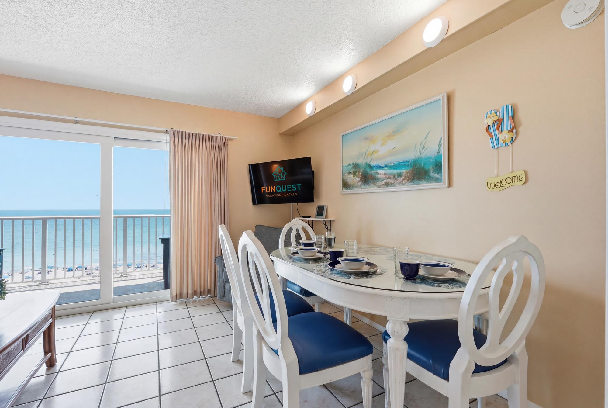 The Summit 830 – Dining area with a table set, ocean view through large sliding glass doors, and a television on the wall.