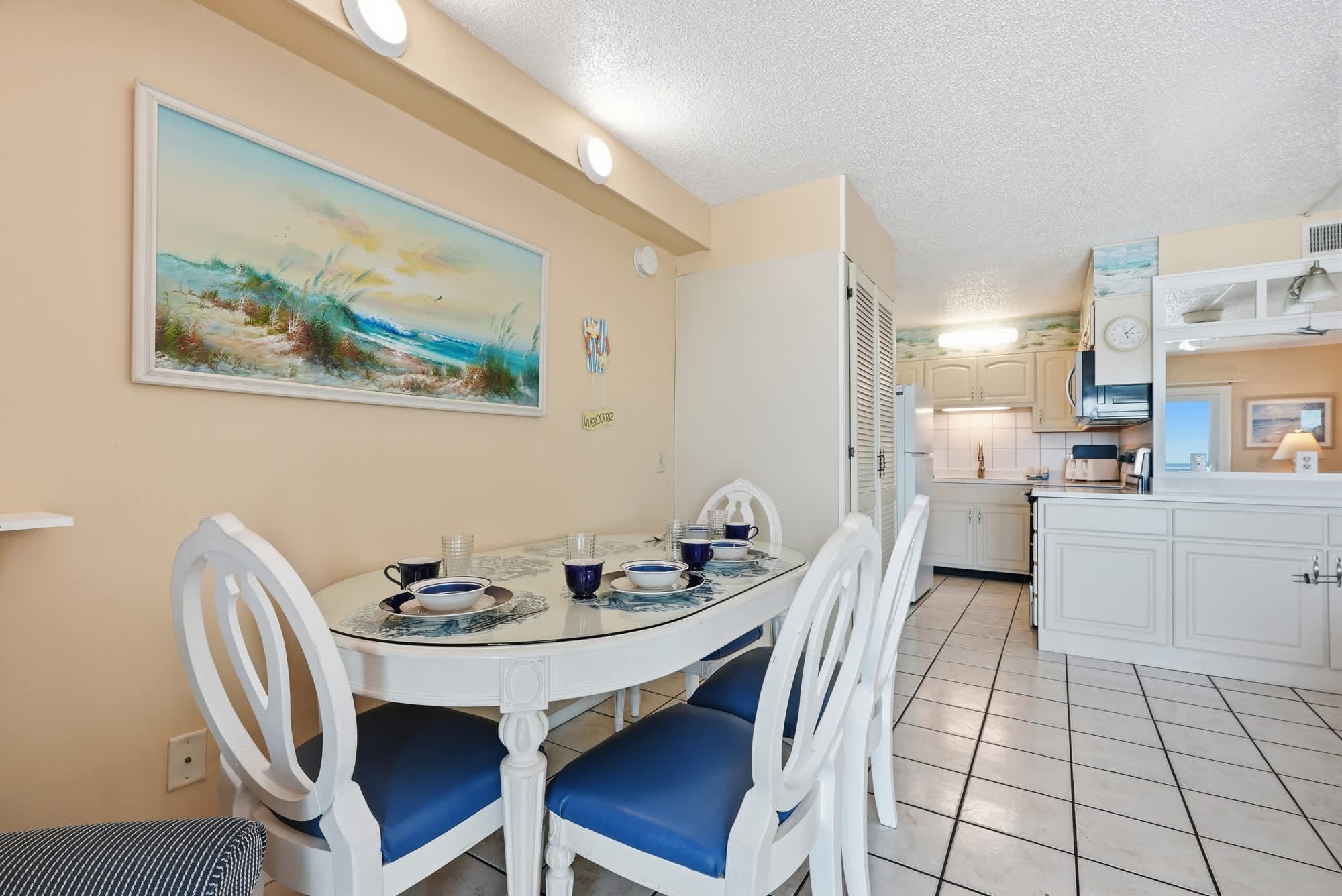 The Summit 830 – Dining area with a white table, blue chairs, and a kitchen visible in the background.