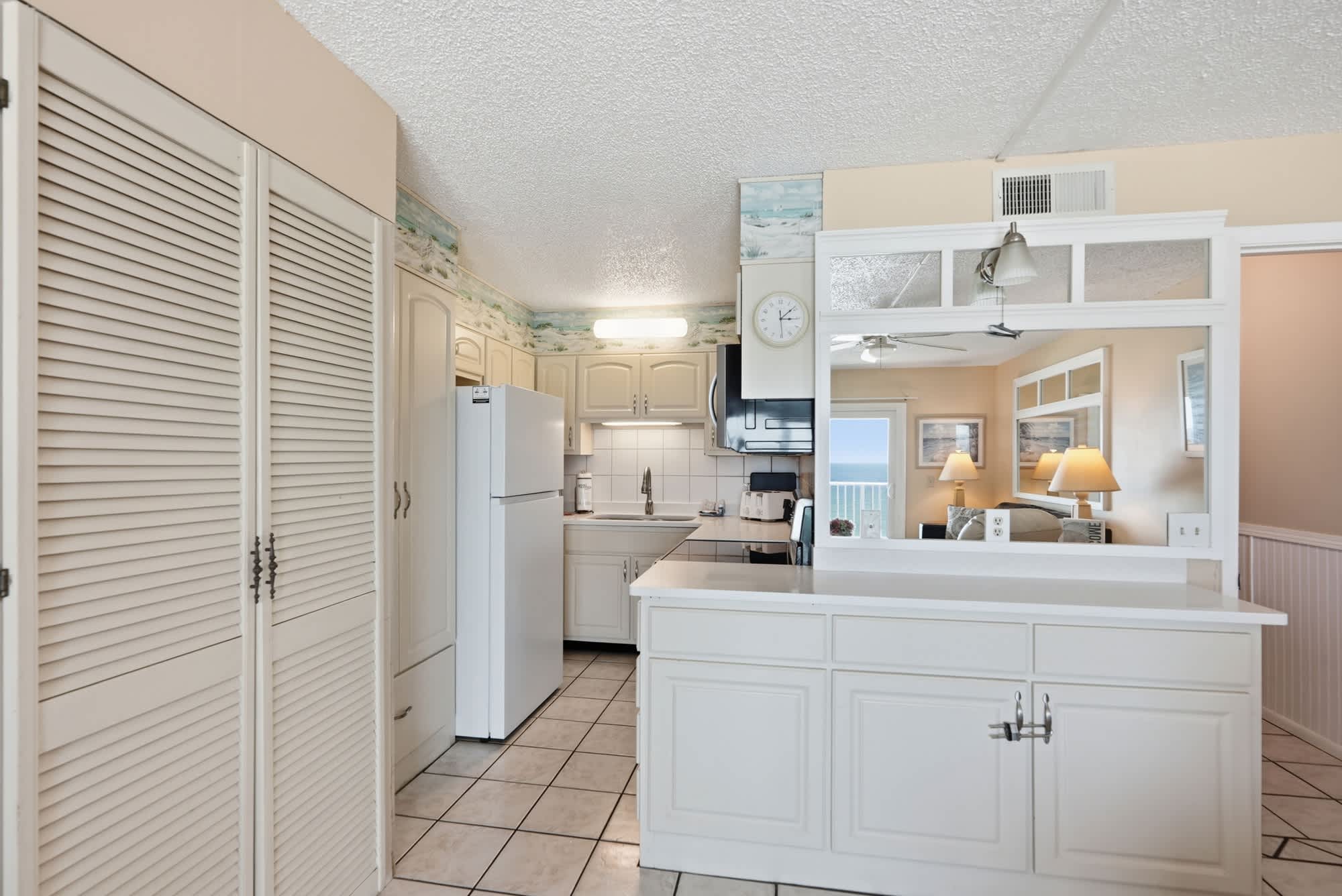 The Summit 830 – Bright kitchen with white cabinets, tiled floor, and a view of the ocean through the window.