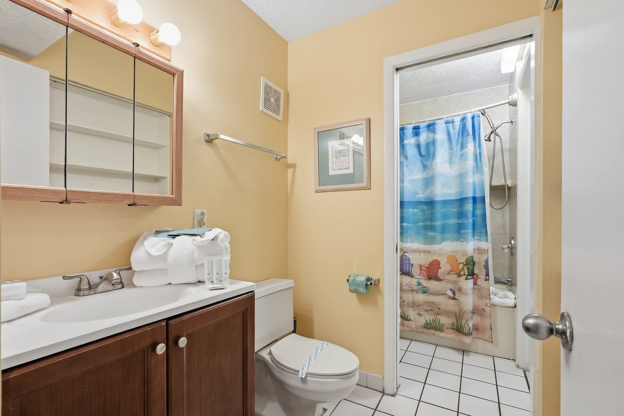 The Summit 830 – Bathroom with yellow walls, sink, mirror, and beach-themed shower curtain.