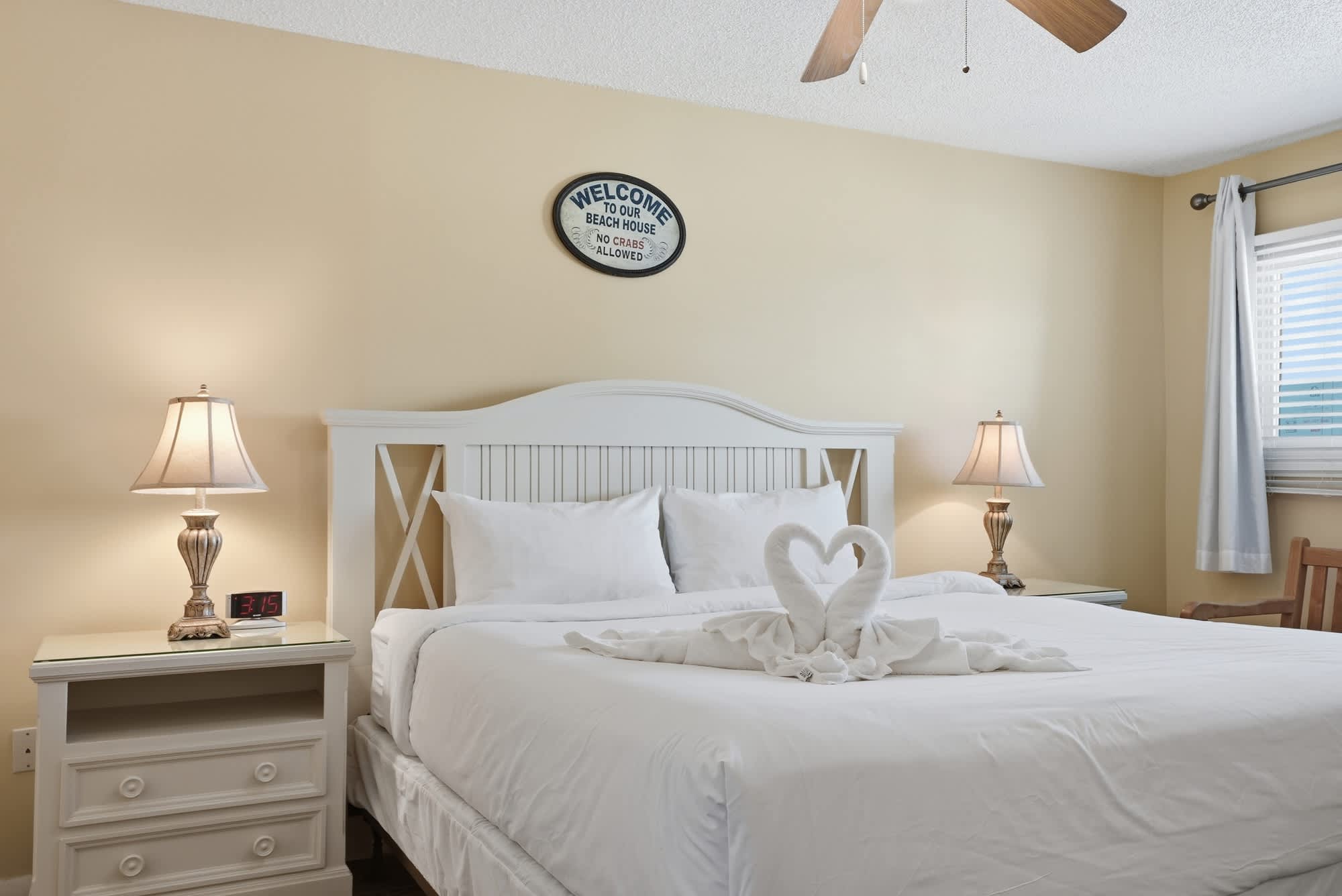 The Summit 830 – Cozy bedroom with a queen bed, decorative towel swans, bedside lamps, and a small window.