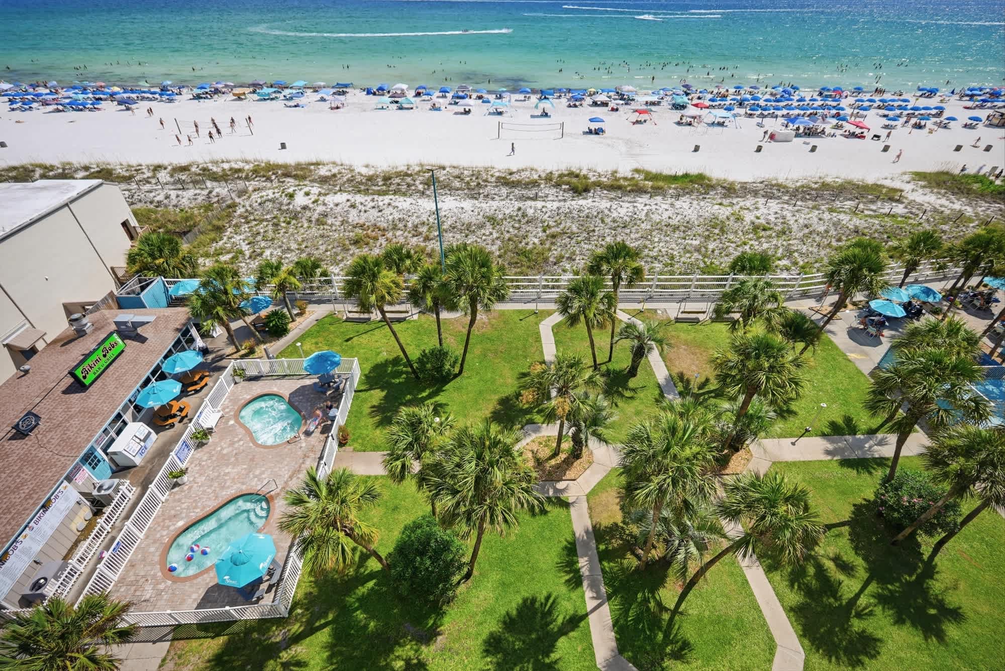 The Summit 830 – Aerial view of a beachfront rental, featuring pools, palm trees, and umbrellas lining the beach.
