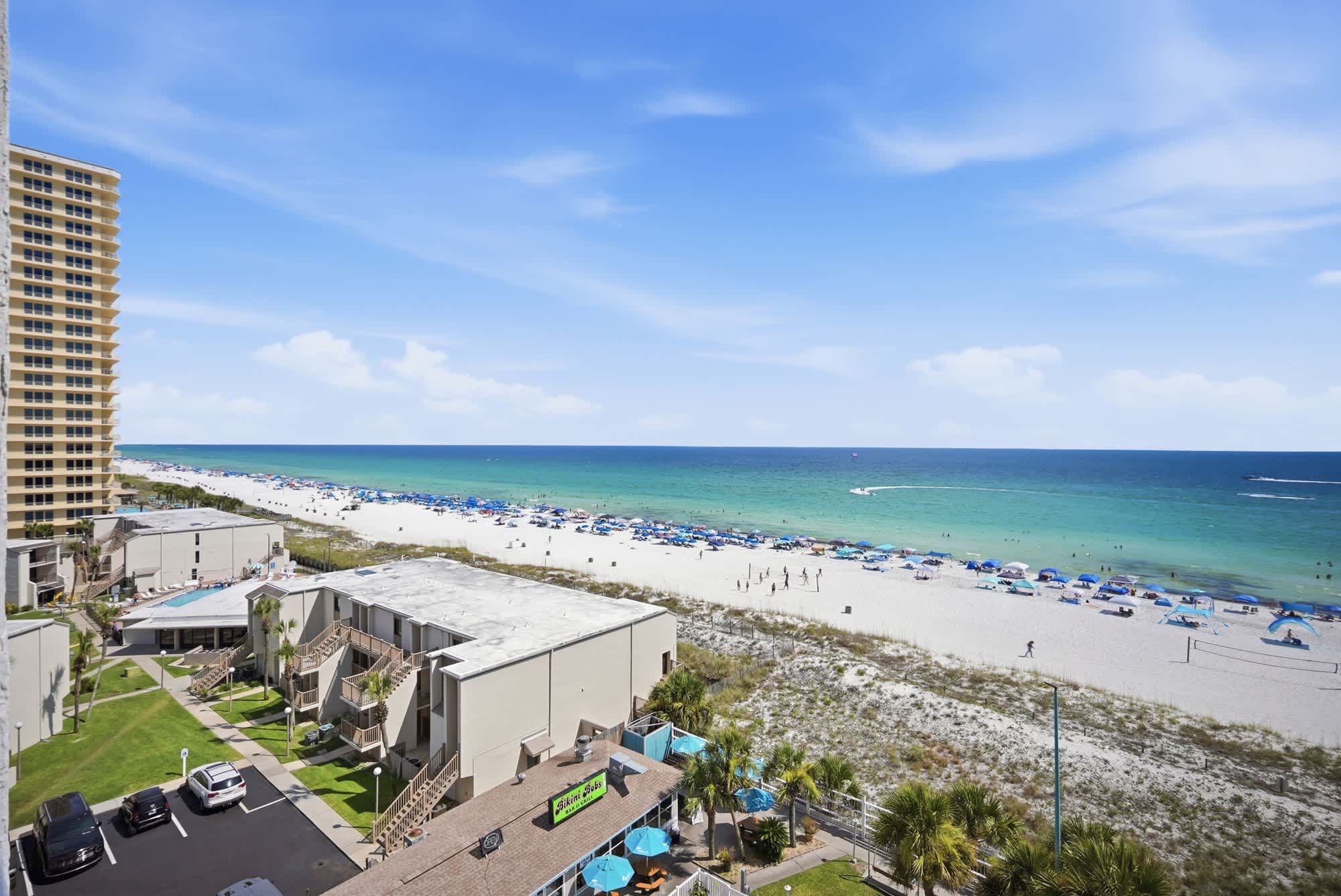 The Summit 830 – View of the beach with umbrellas, green water, and nearby buildings from a high vantage point.