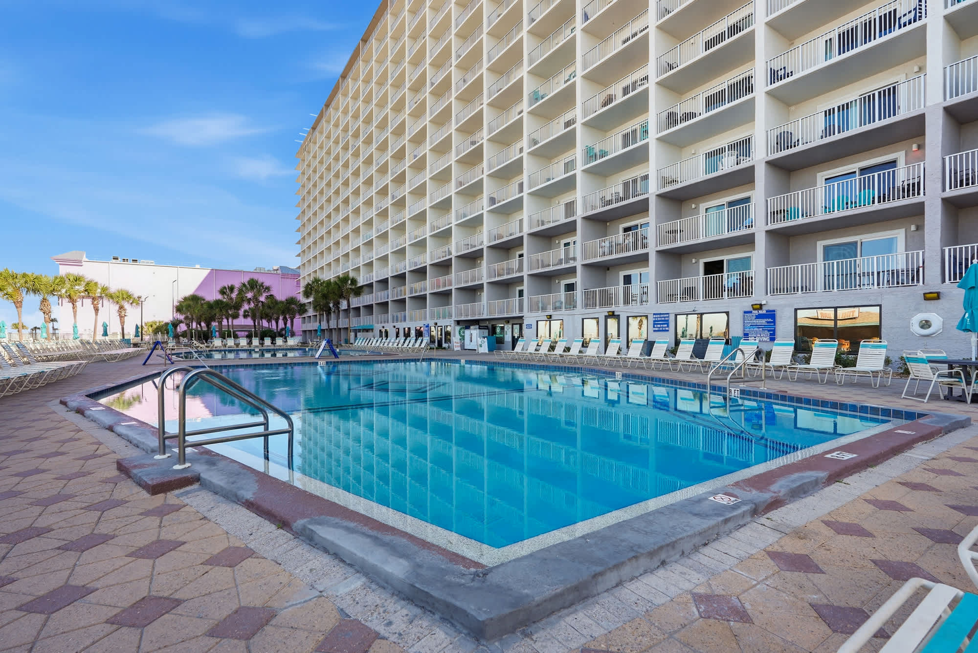 The Summit 830 – Swimming pool with lounge chairs, surrounded by a multi-story building and palm trees.
